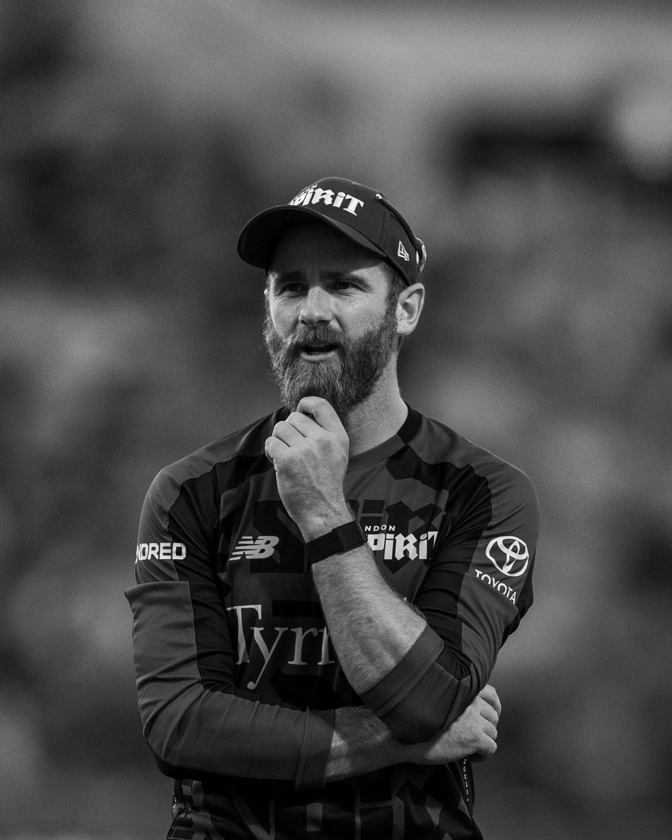 A man with a beard, wearing a cap and sportswear, standing outdoors with arms crossed, looking thoughtful.
