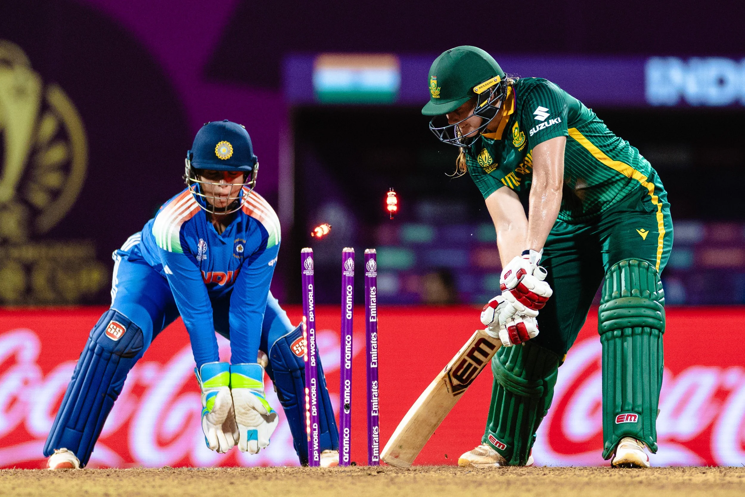 Cricket players from India and South Africa during a match, with the South African player preparing to bat and the Indian wicketkeeper crouching behind the stumps.