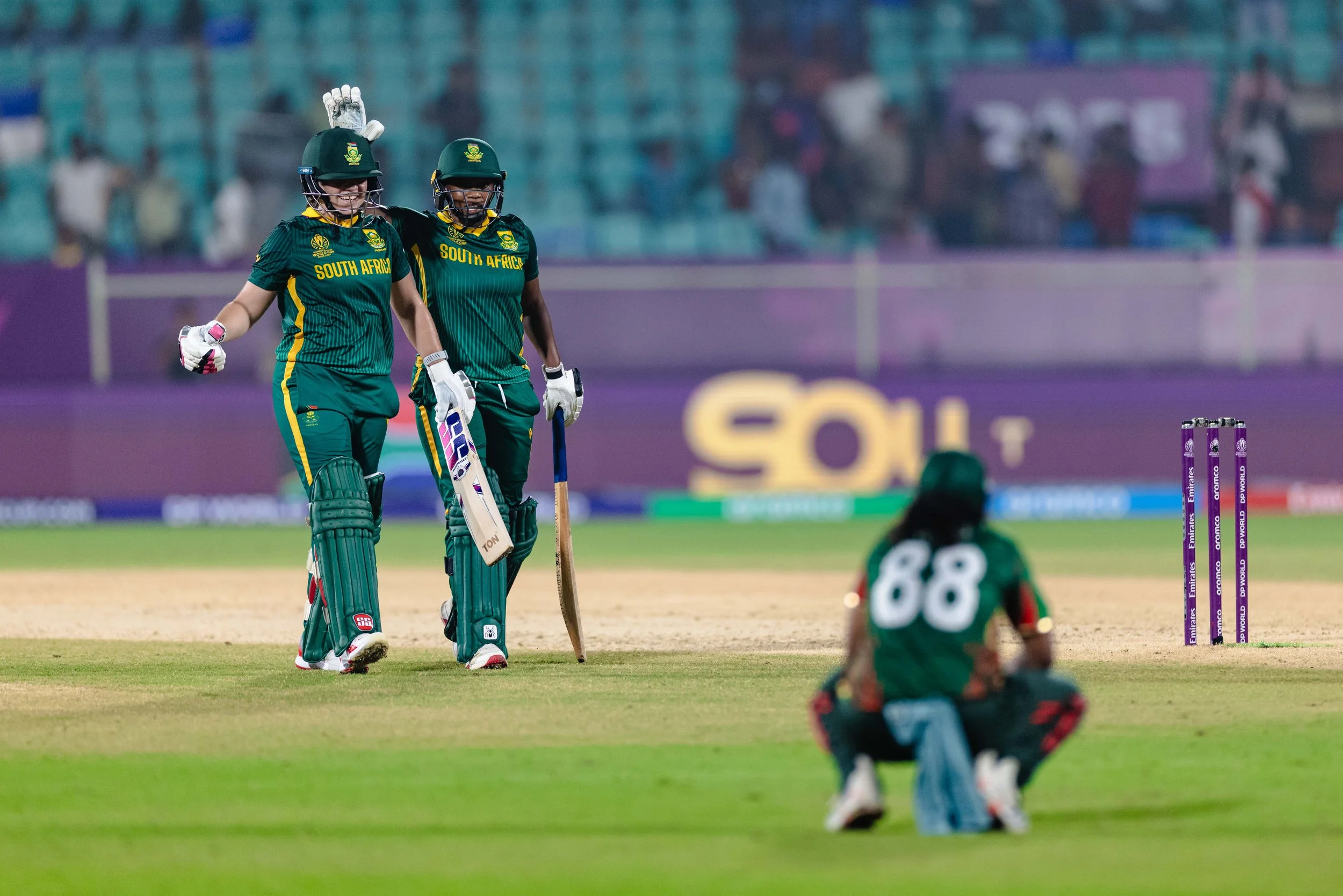 South African female cricket players celebrating on the field during a match, with the bowler in foreground and the stumps visible.