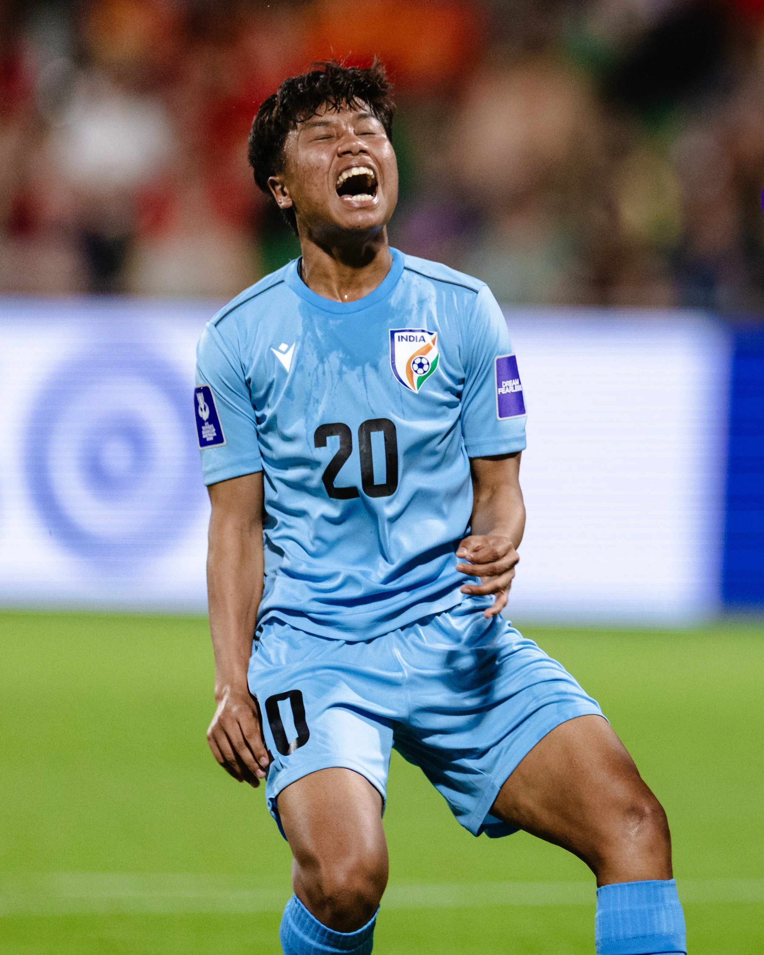 Indian male soccer player in a light blue uniform, number 20, on the field, appearing to be celebrating or expressing emotion.