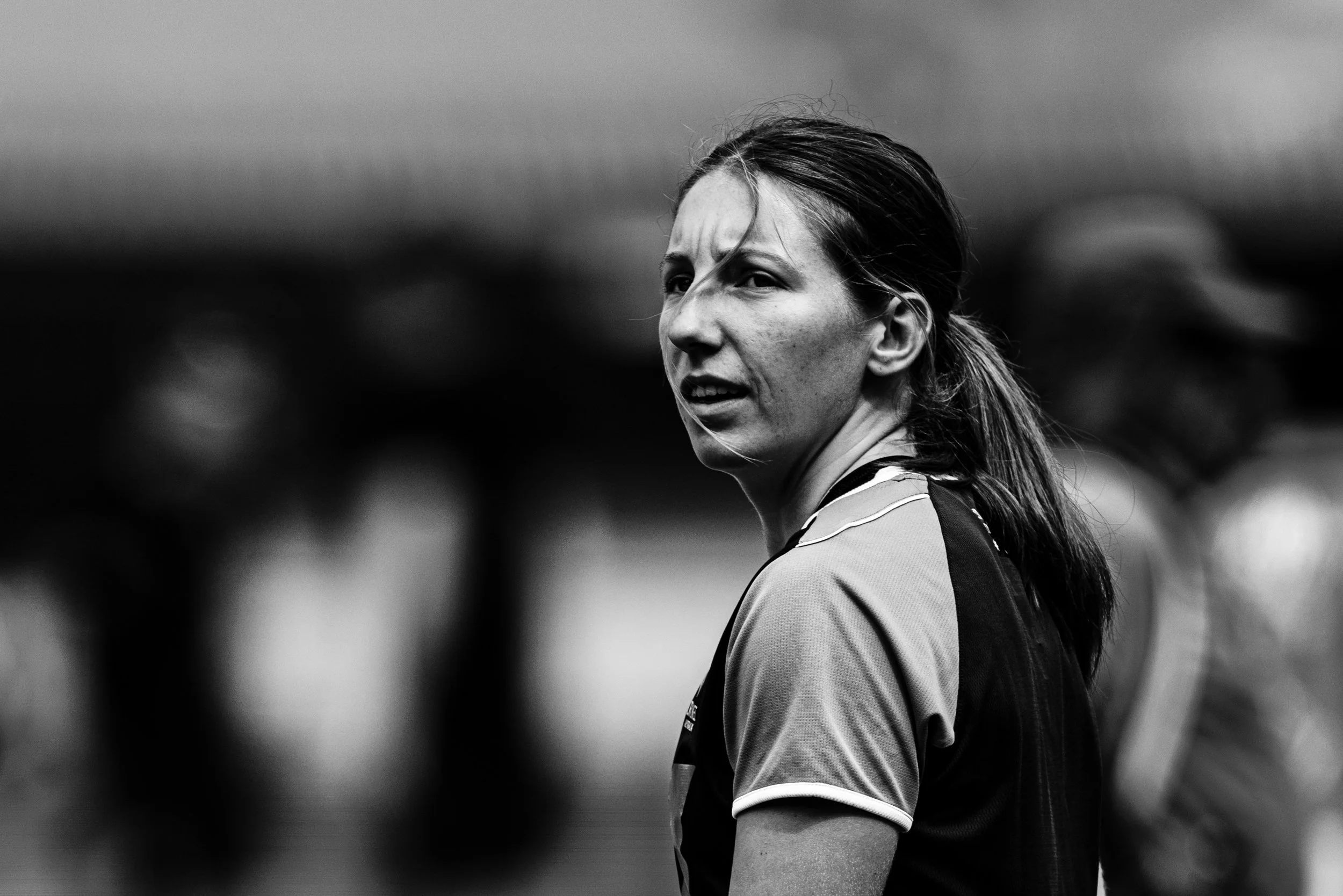 Black and white photo of a woman with long hair pulled back, wearing a sports jersey, looking to her left with a serious expression.
