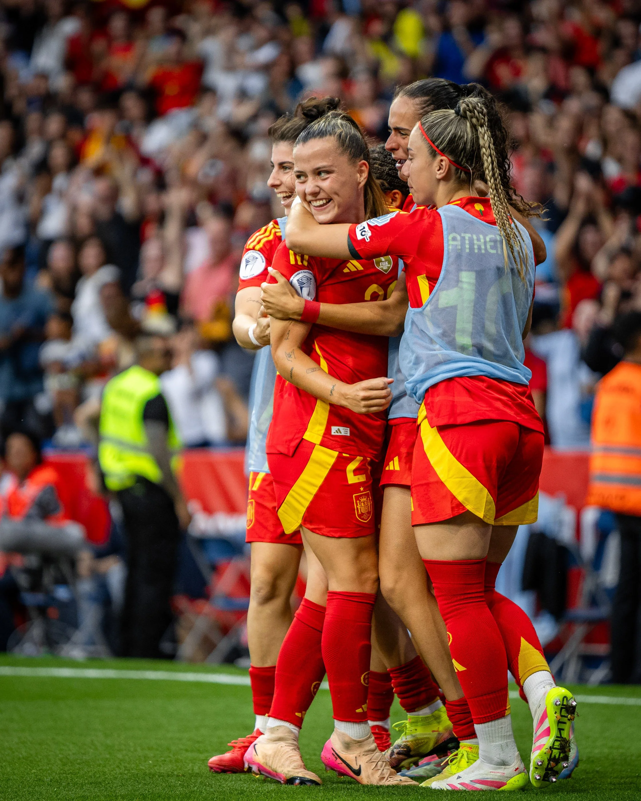 Soccer players in red uniforms embracing on the field during a match, with a crowd of spectators in the background.