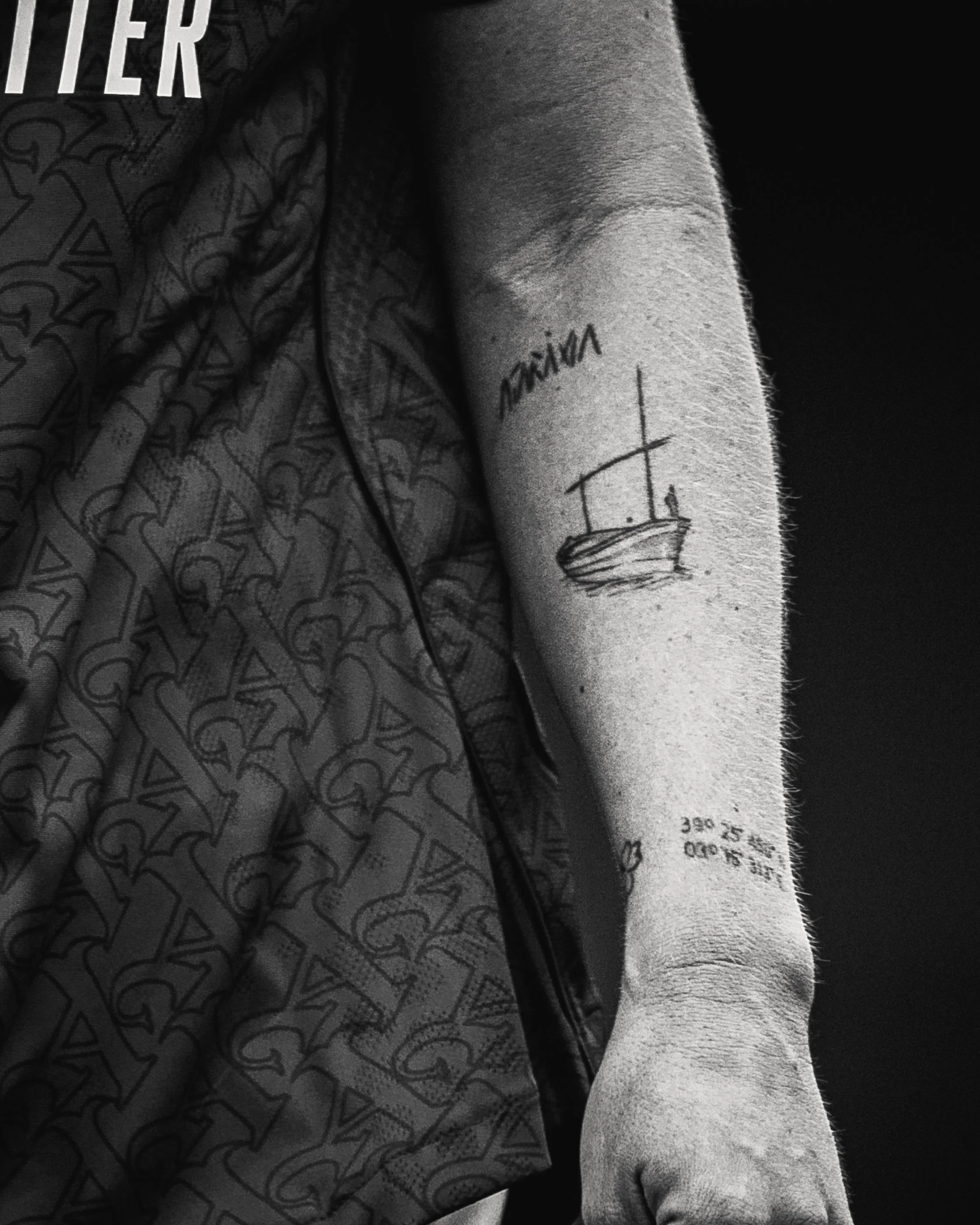 Close-up of a person’s arm showing a tattoo of a ship and the name 'Victoria' written above it, with part of their clothing visible.