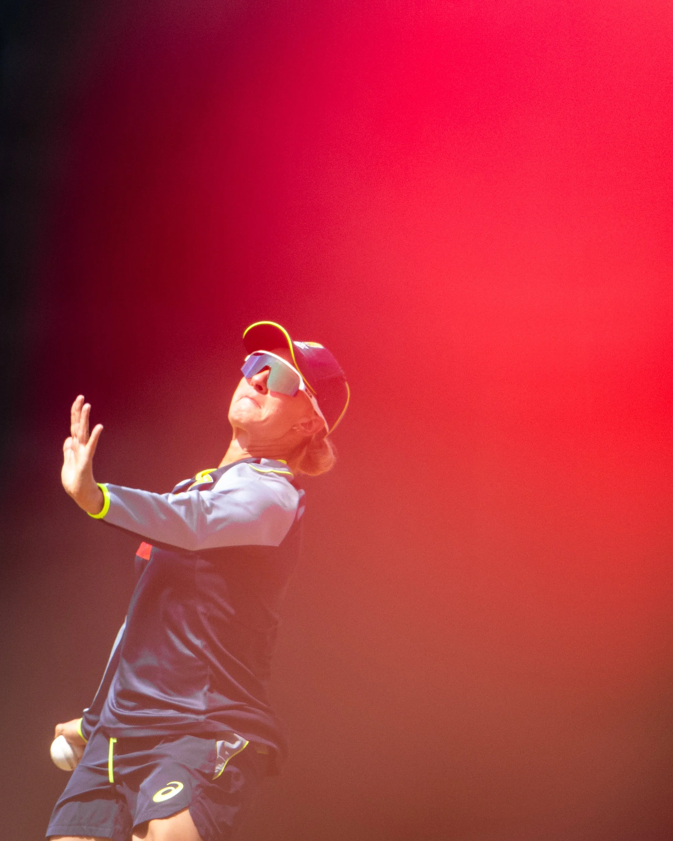 A tennis player wearing a visor and sunglasses, captured in mid-swing against a red background.