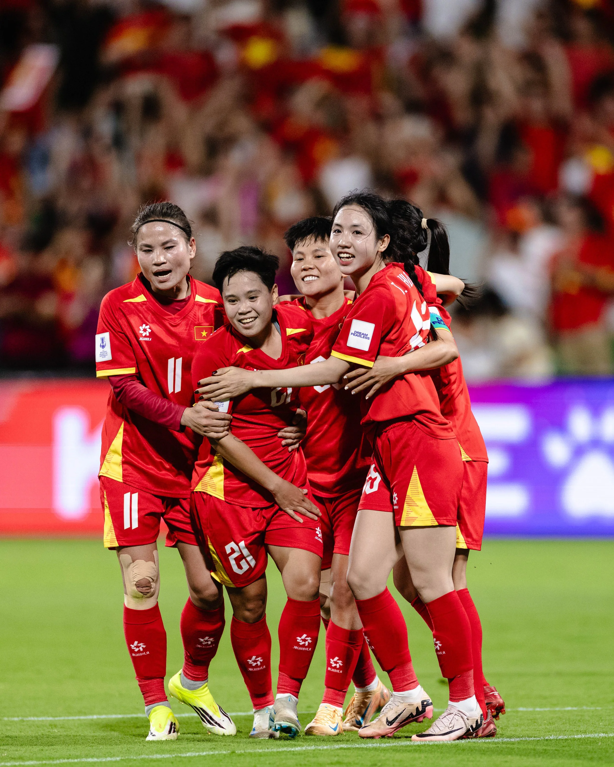 A group of female soccer players wearing red uniforms, hugging and celebrating on the field.