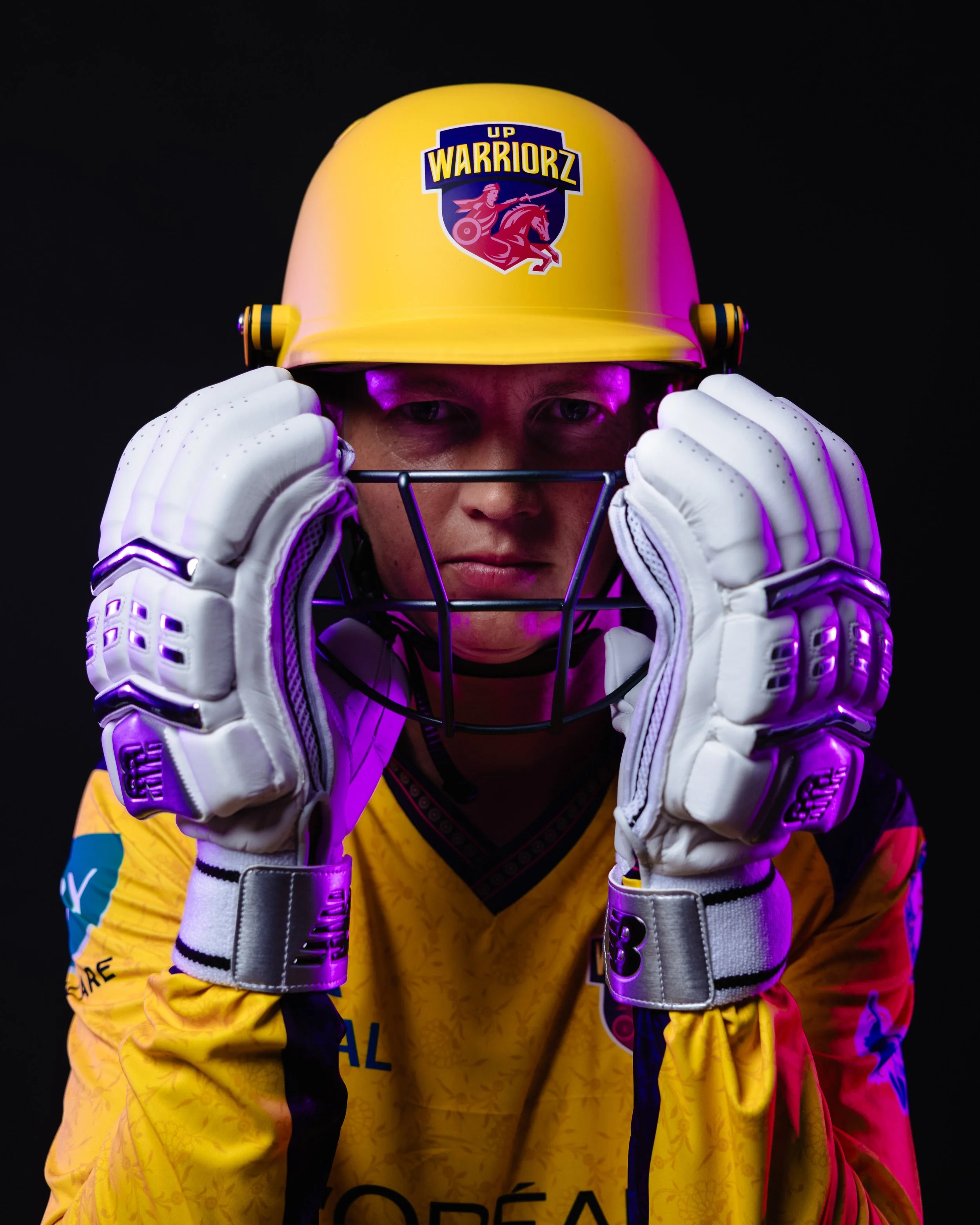 A person wearing yellow hockey jersey and gloves, adjusting a yellow hockey helmet with a UP WarriorZ logo, against a dark background.