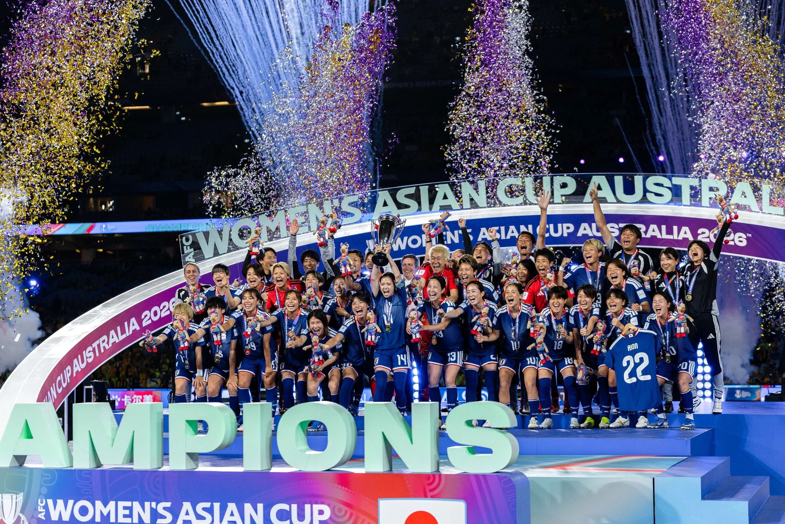 Celebrating soccer team winning the Women's Asian Cup at a trophy ceremony with confetti, fireworks, and a cheering crowd.