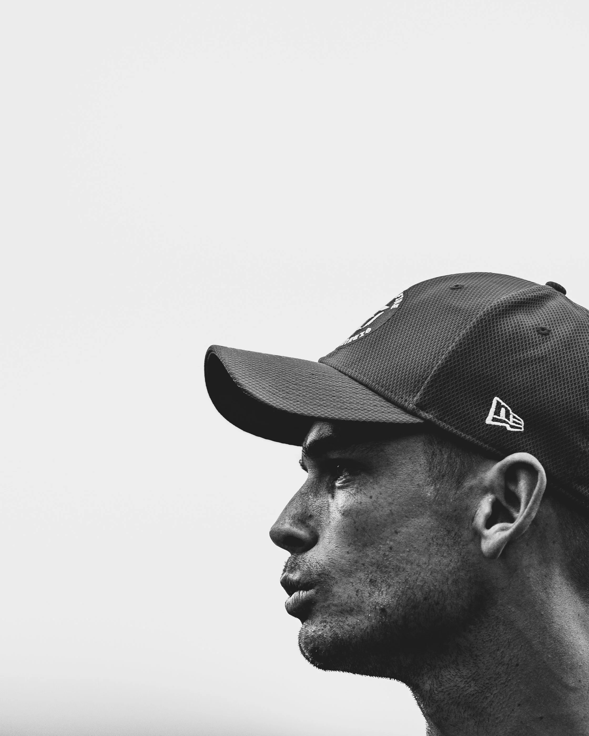 Side profile of a young man wearing a black cap, looking downward, with a neutral expression, against a plain light background.