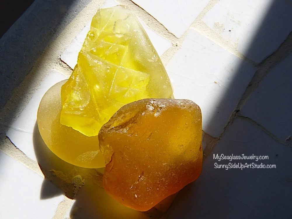 Two pieces of raw amber resin, one yellow and one orange, placed on a white tiled surface in sunlight.