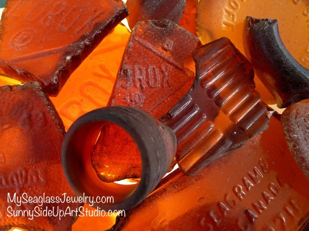 Close-up of brown glass bottles, some with embossed text, and one with a ridged black cap, arranged closely with warm lighting.