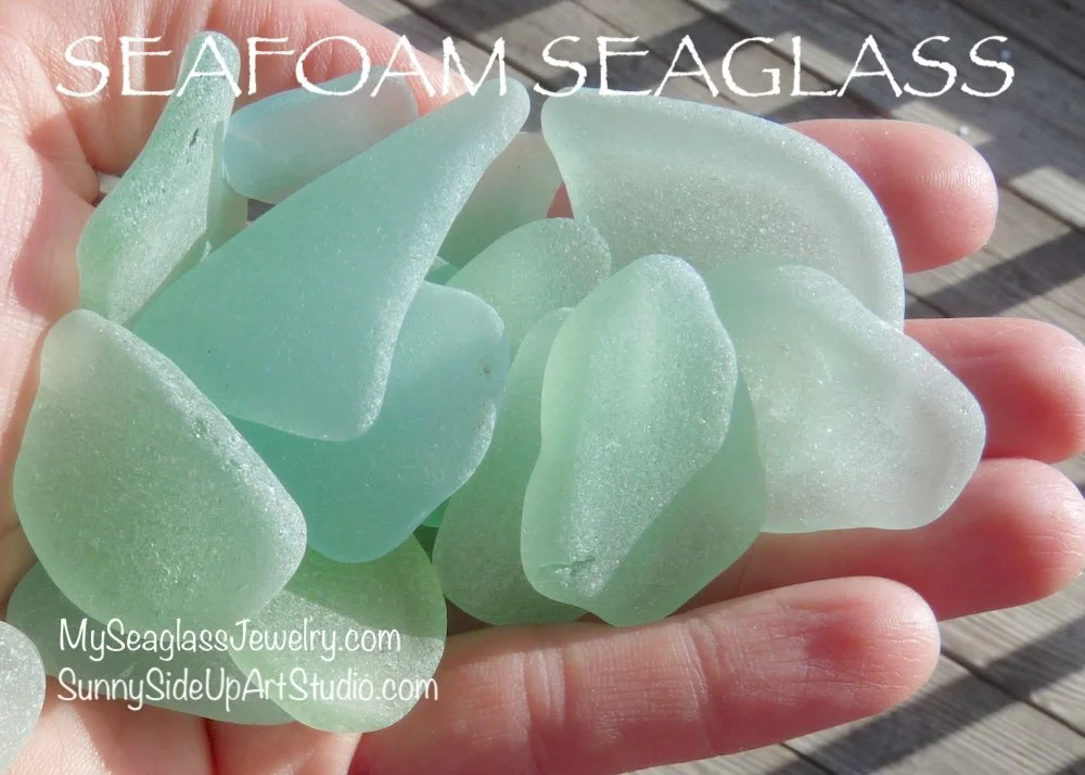 A person holding seafoam green sea glass pieces over a wooden surface. Text on the image reads "Seafoam Seaglass" and includes website URLs.