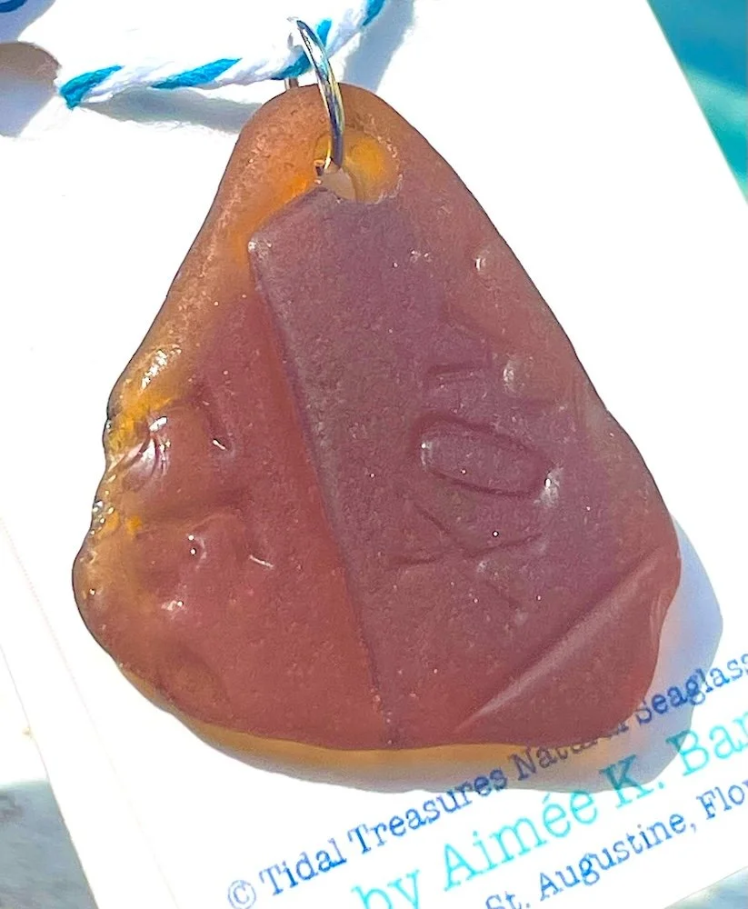 A frosty honey brown seaglass pendant with the embossed word 'Clorox' hanging from a blue and white string.