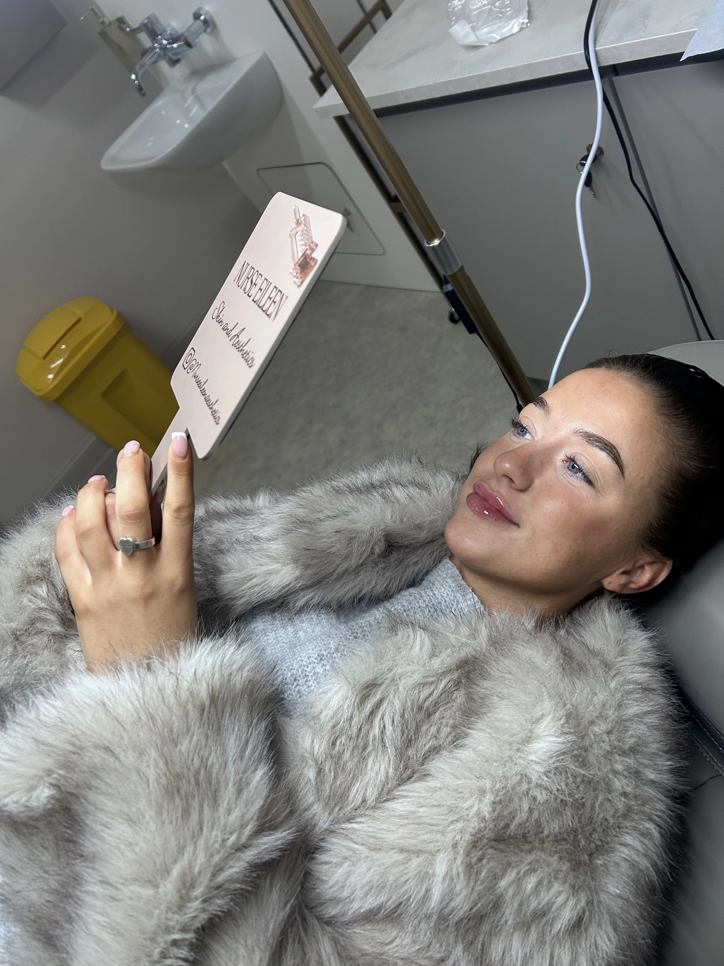 A woman lying in a medical setting, holding a sign that says 'NURSEELIEN, Sleep and Relaxation' with a picture of a building, while connected to medical equipment.