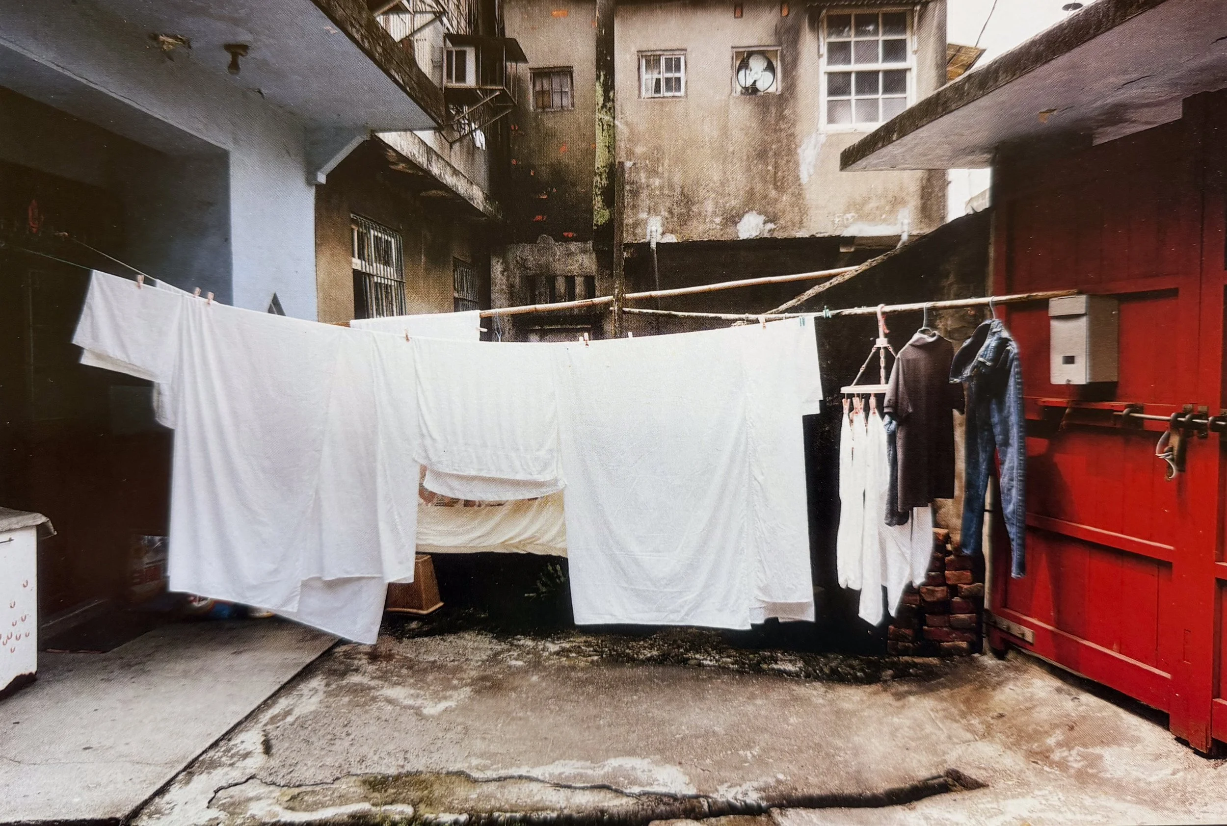 An apartment courtyard with laundry hanging on a clothesline, a red door, and multiple worn buildings with windows and balconies, photographed by visual artist, Karen Serago.