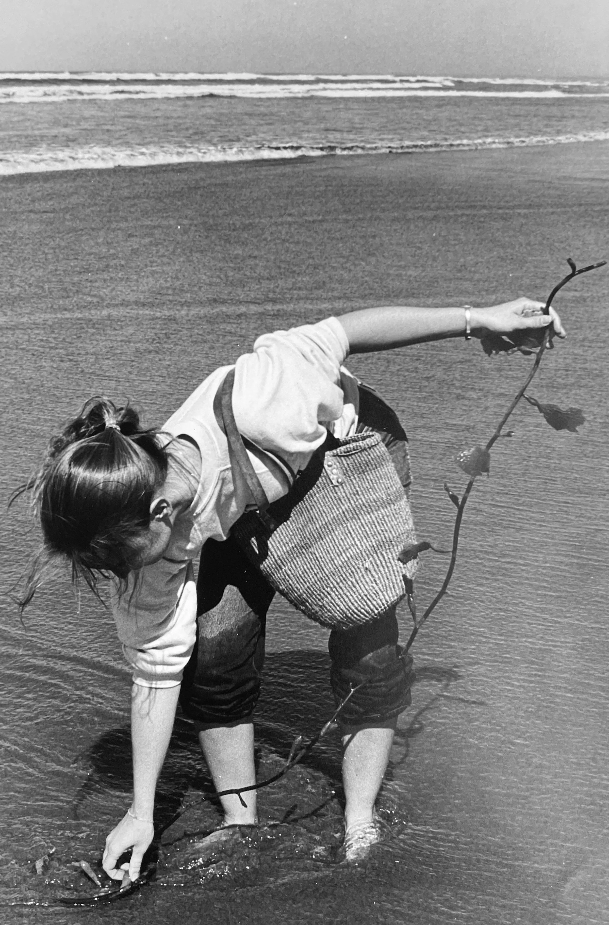 A woman bending over in shallow water by the beach, holding fishing lines into the water,  photographed by visual artist, Karen Serago.