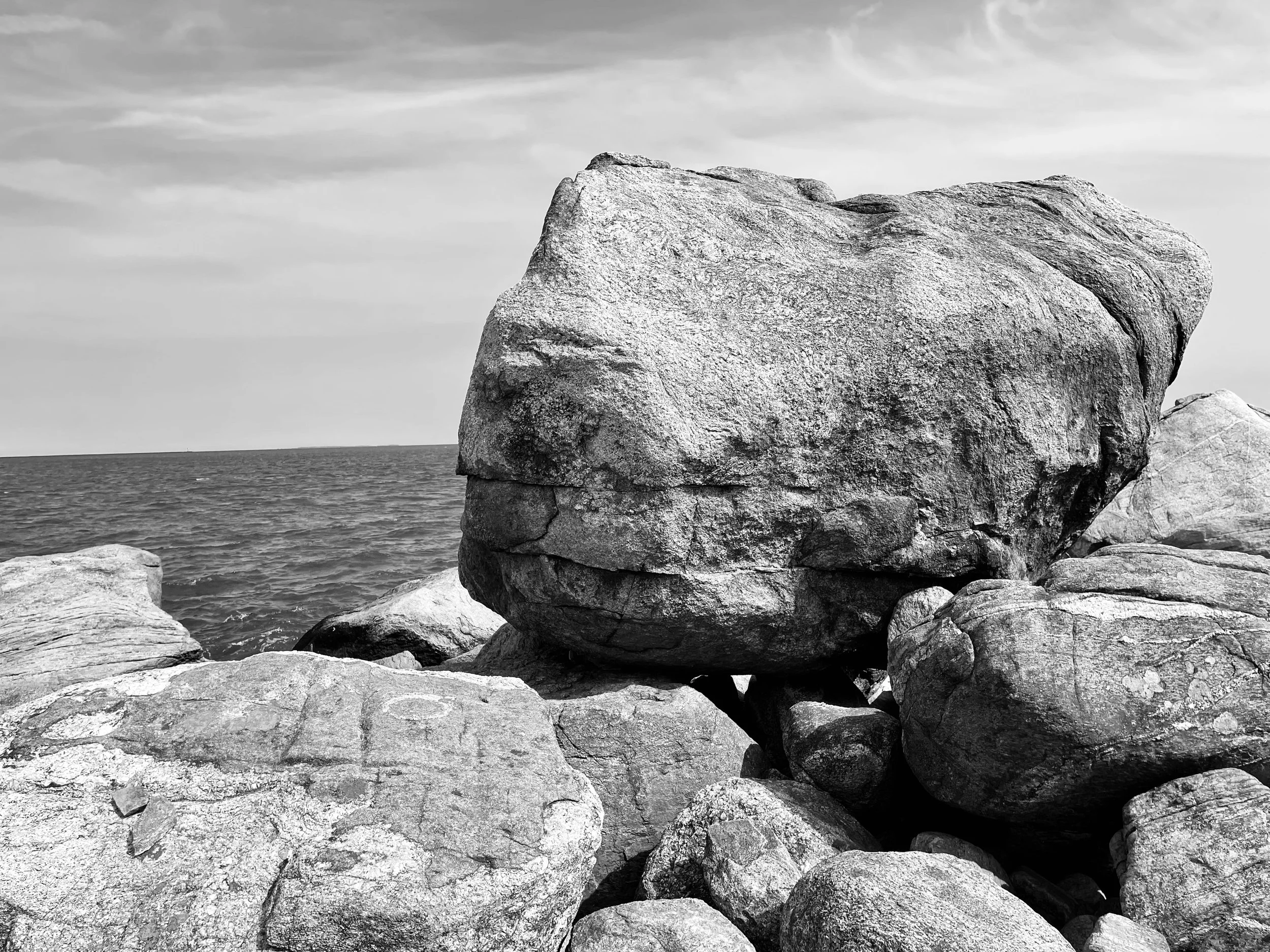 Large rock formations near the shoreline with water and sky in the background photographed by visual artist, Karen Serago.