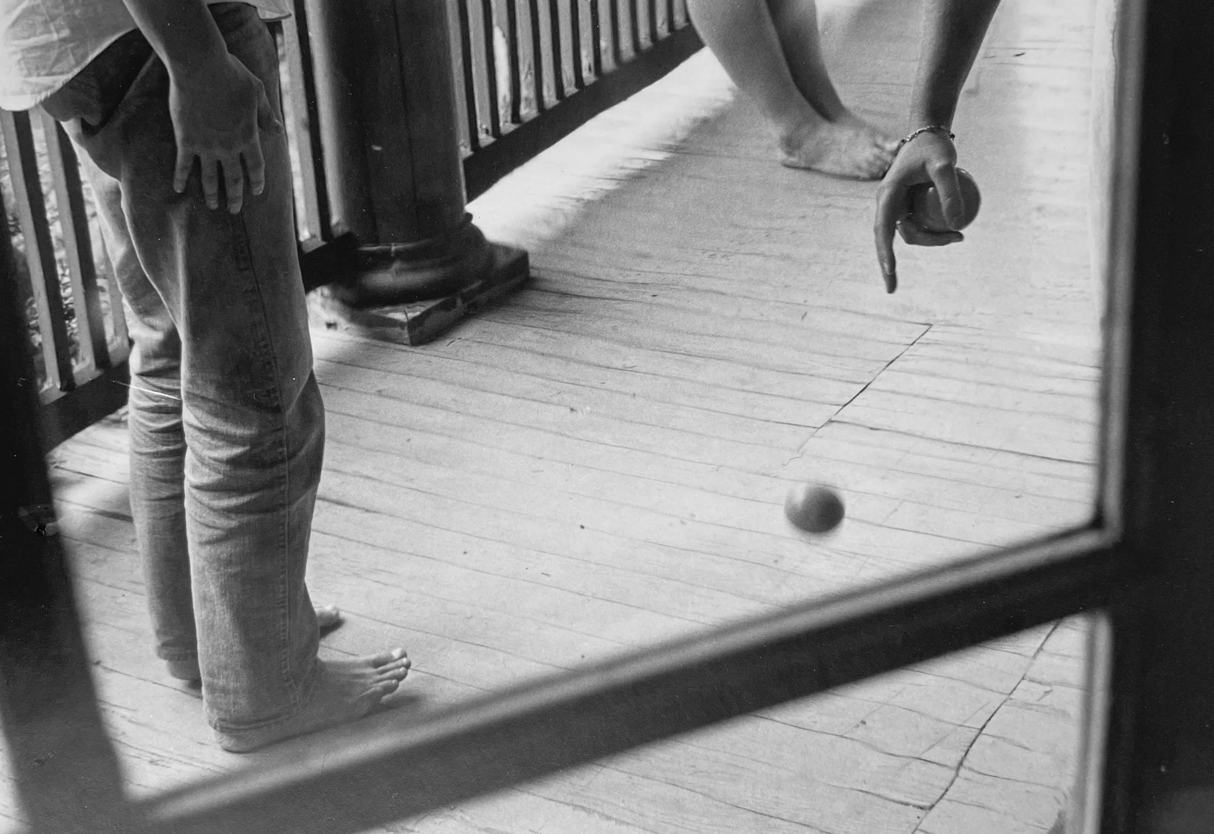 A person standing barefoot on a wooden floor playing street hockey, holding a hockey stick with a ball near the stick's blade, photographed by visual artist, Karen Serago.