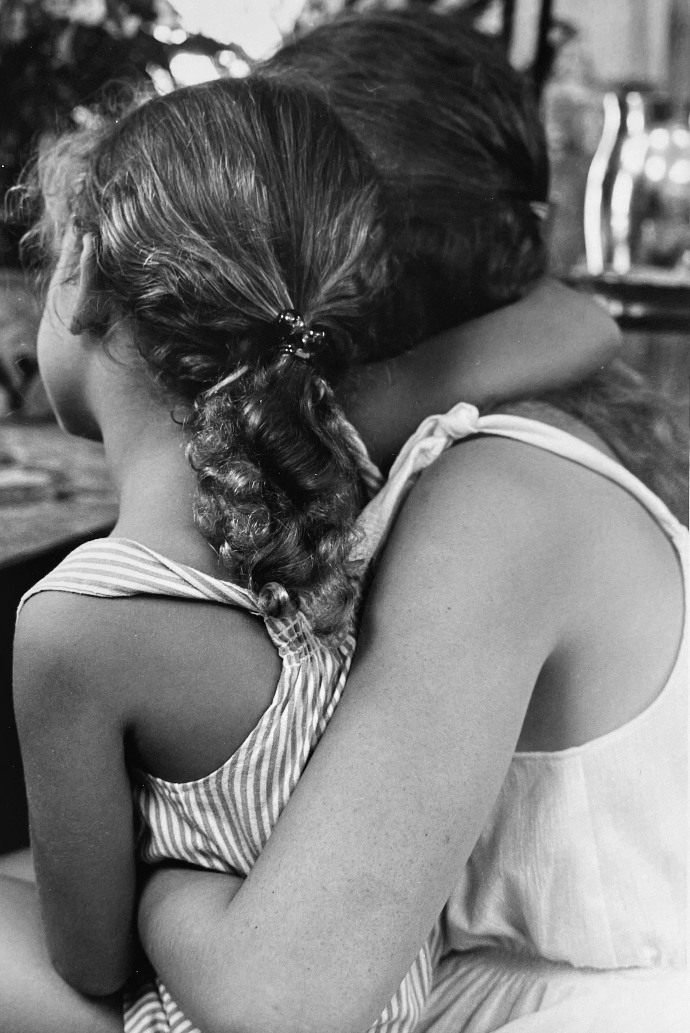 Close-up of two children embracing each other, one with braided hair and the other with straight hair, wearing striped shirts, in black and white, photographed by visual artist, Karen Serago.