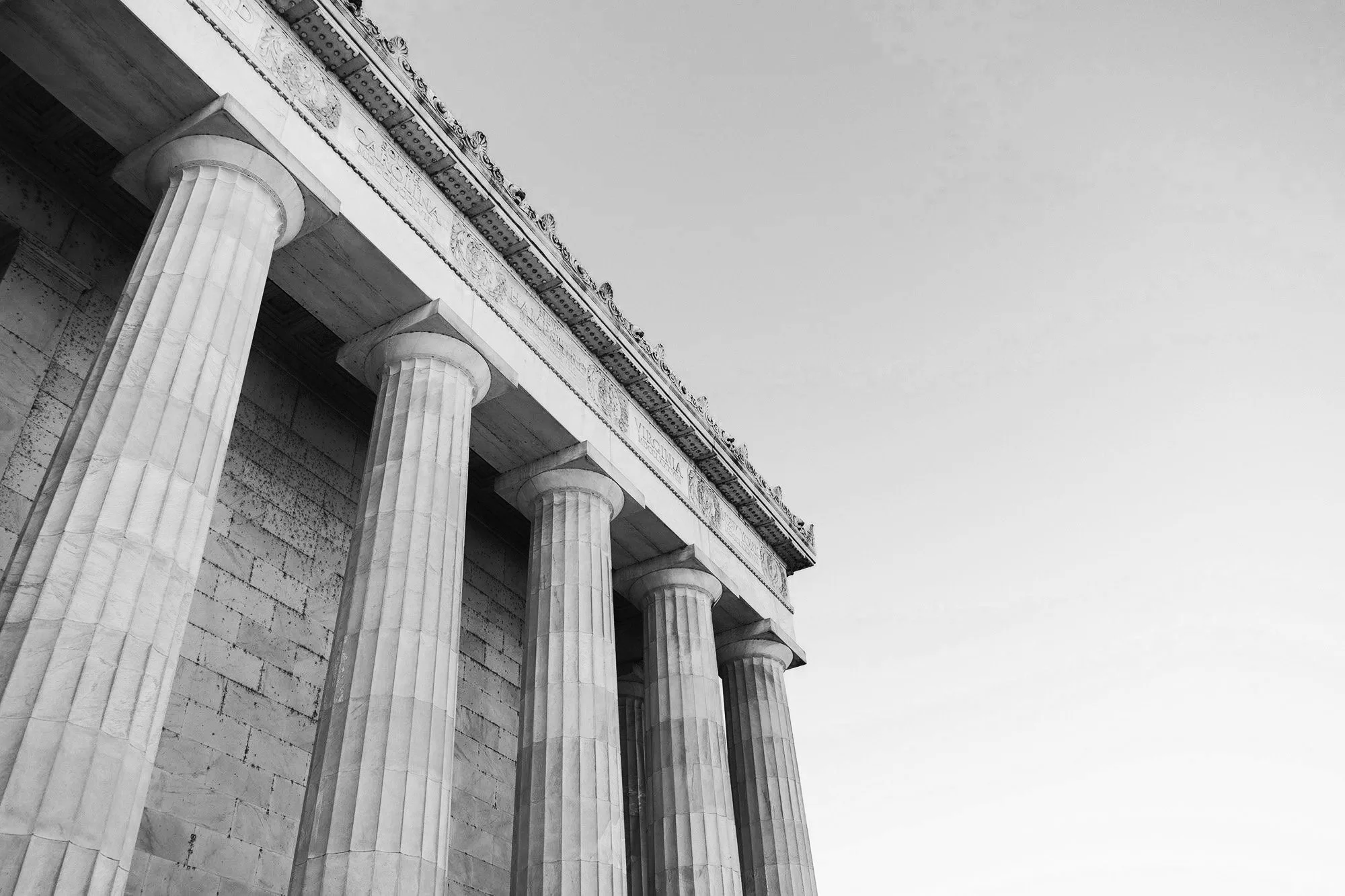 Close-up of the columns and entablature of the Parthenon temple in Athens, Greece, shown from an upward angle in black and white.