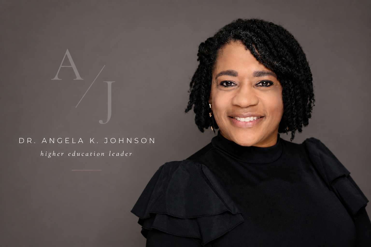 Portrait of Dr. Angela K. Johnson, a higher education leader, smiling against a gray background, wearing a black top with ruffled shoulders.