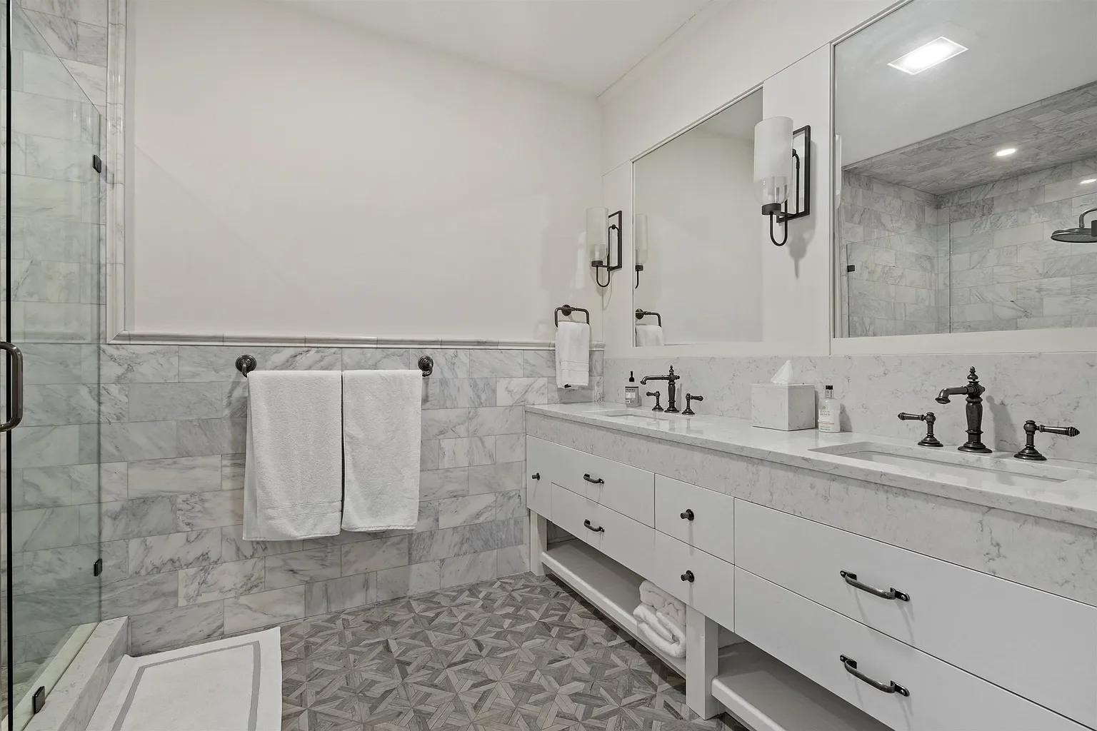Modern bathroom with marble accents, dual sinks, large mirror, shower stall, and towel racks.