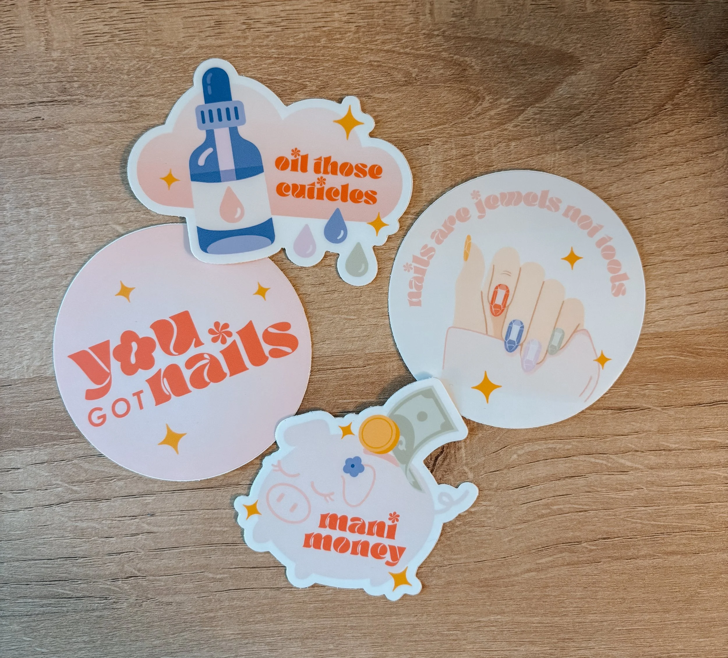 Sticker with a blue and white dropper bottle and orange text that says 'oil those cuticles' on a wooden surface.