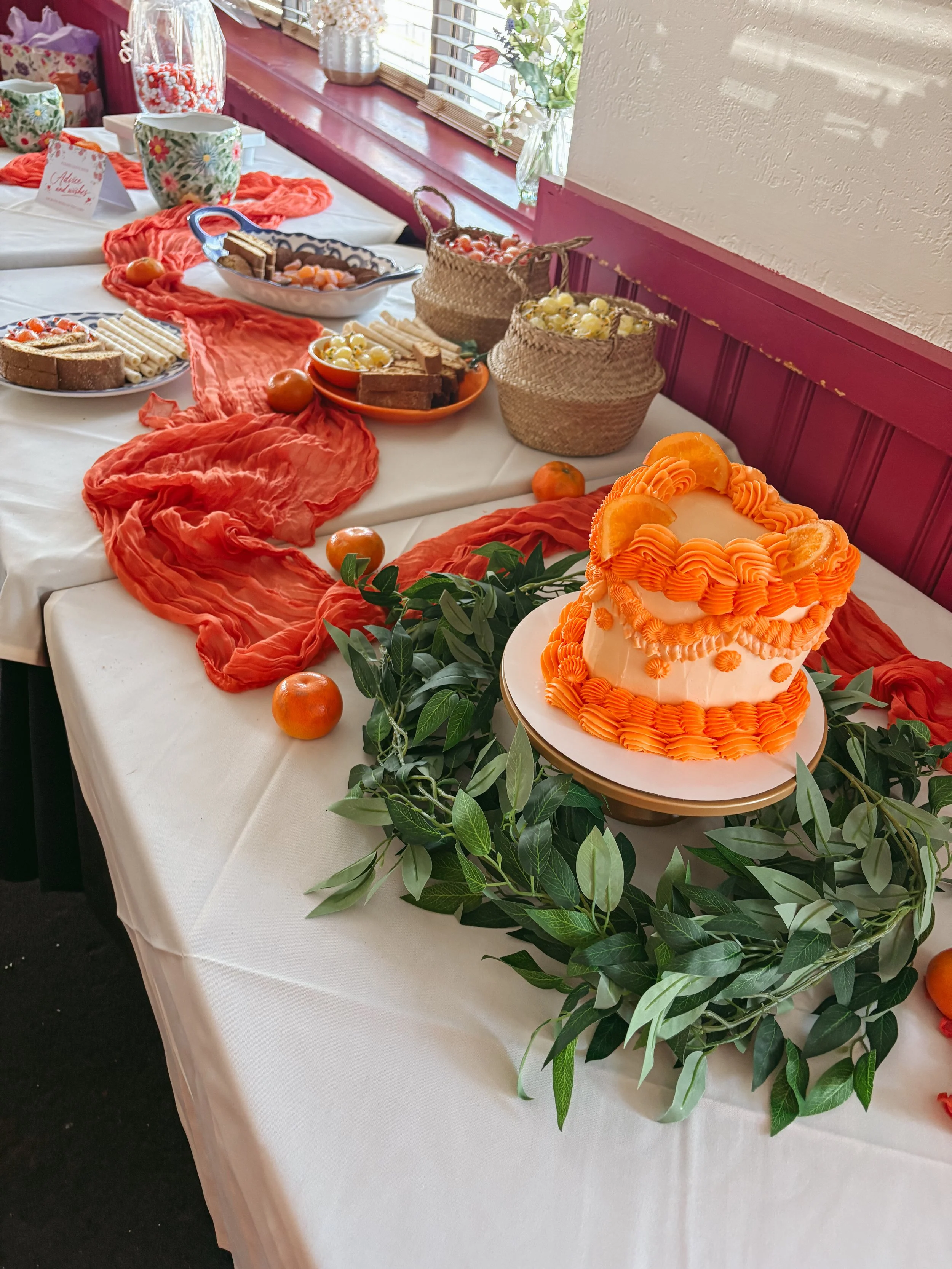 A decorated table with a white tablecloth displaying a cake, bread, fruit, and floral arrangements for a celebration.