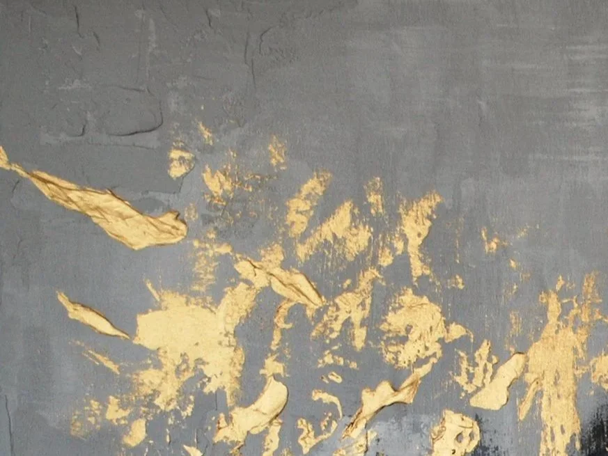 Close-up of a damaged wall with peeling gray paint revealing a gold-colored surface underneath.