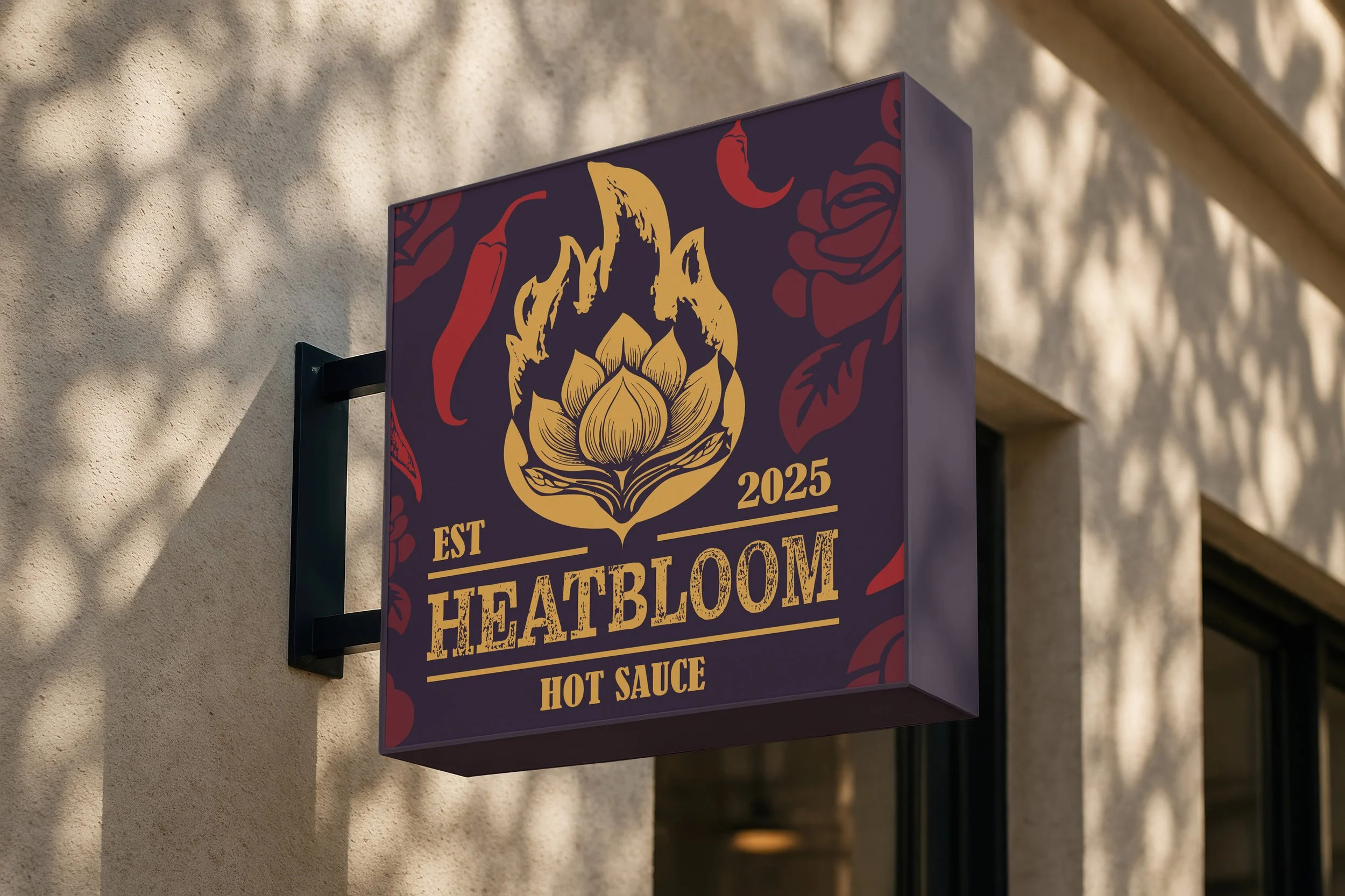 A rectangular sign with a purple background mounted on a beige wall, featuring a golden lotus flower and the words "HEATBLOOM" in large yellow letters, along with "EST 2025" and "HOT SAUCE" in smaller yellow text, decorated with red floral accents.