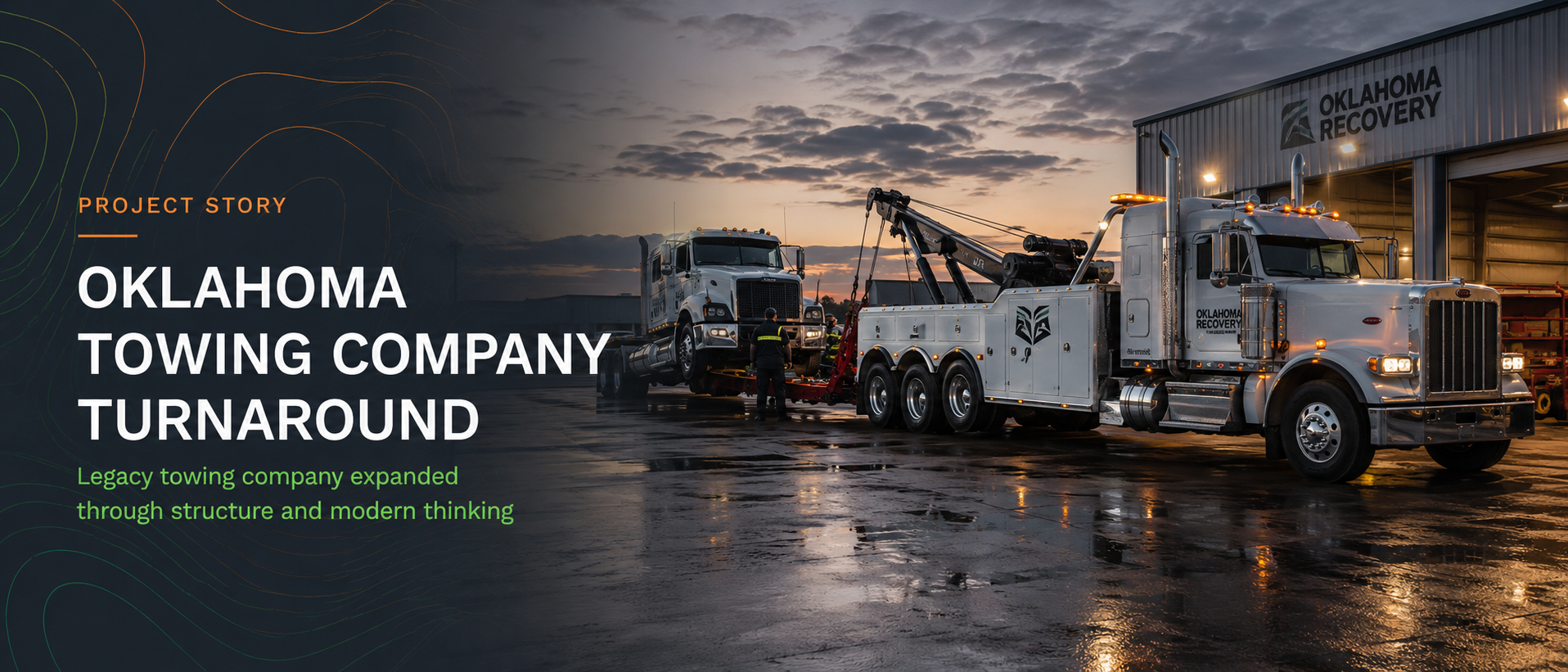 A tow truck from Oklahoma Recovery is towing a semi-truck inside a warehouse, with a sunset sky in the background.