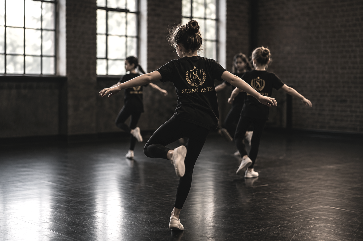 Young girls practicing ballet or dance in a studio with brick walls and large windows.