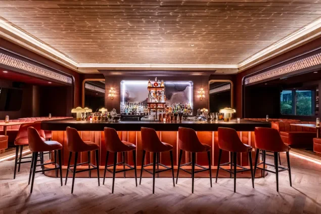 Elegant modern bar with a curved counter, red barstools, and a well-stocked back bar with bottles and glassware, decorated with warm lighting.
