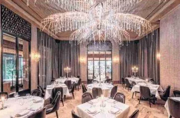 Elegant dining room with round tables, black and gray chairs, and a large chandelier, with large windows and curtains.