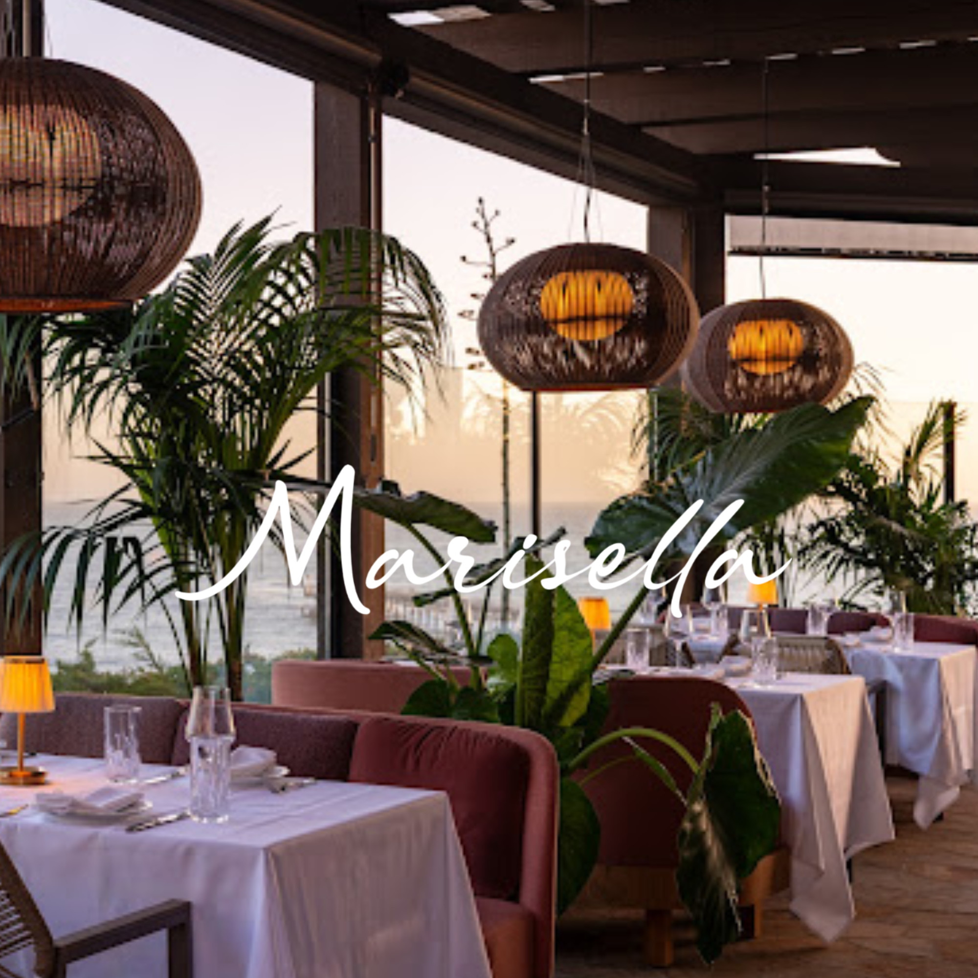 Indoor dining area with white tablecloths, pink chairs, large potted plants, and hanging wicker pendant lights, possibly at a restaurant or event space.