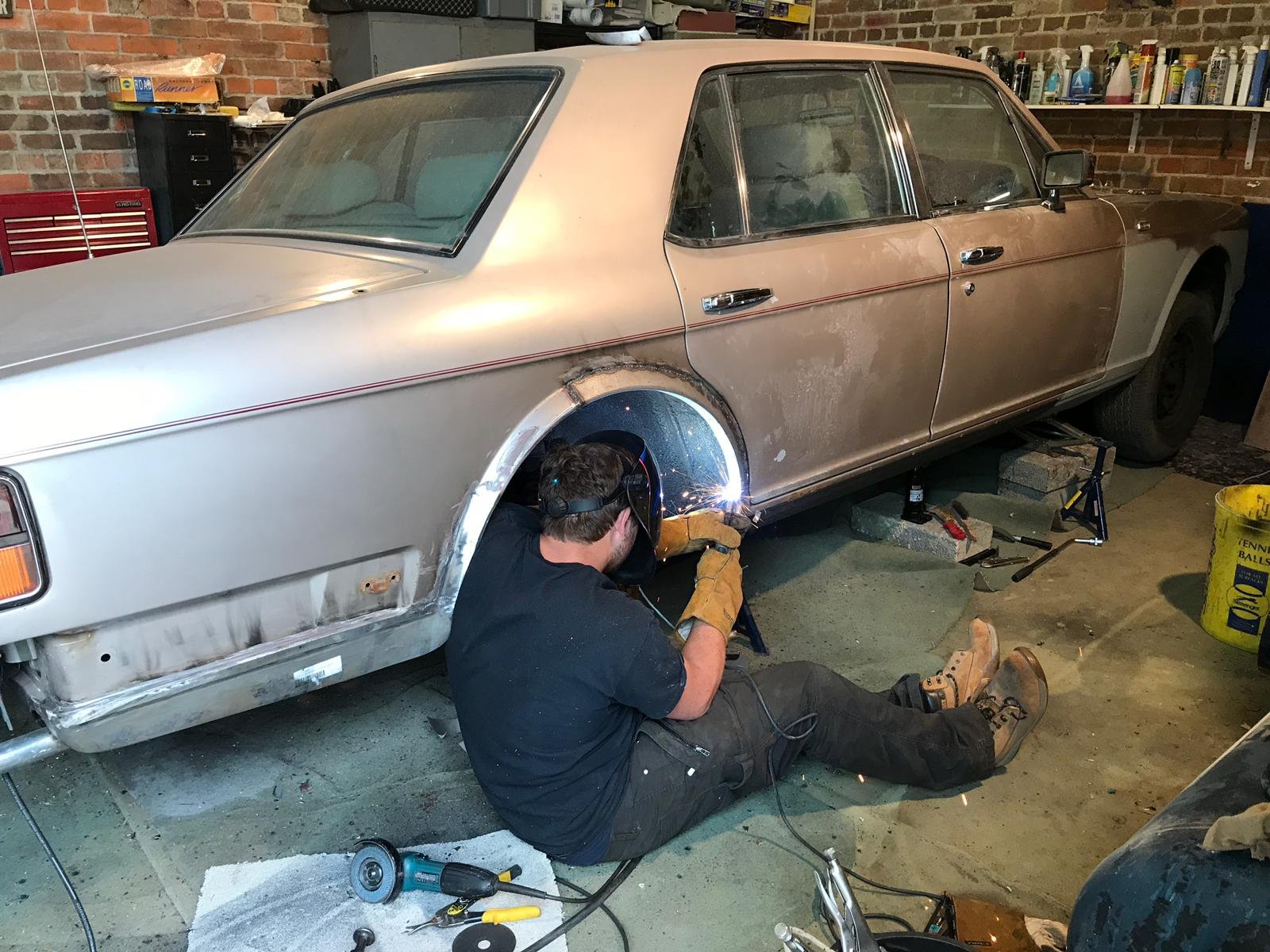 A person welding a vintage car in a garage workshop, with tools and equipment around.