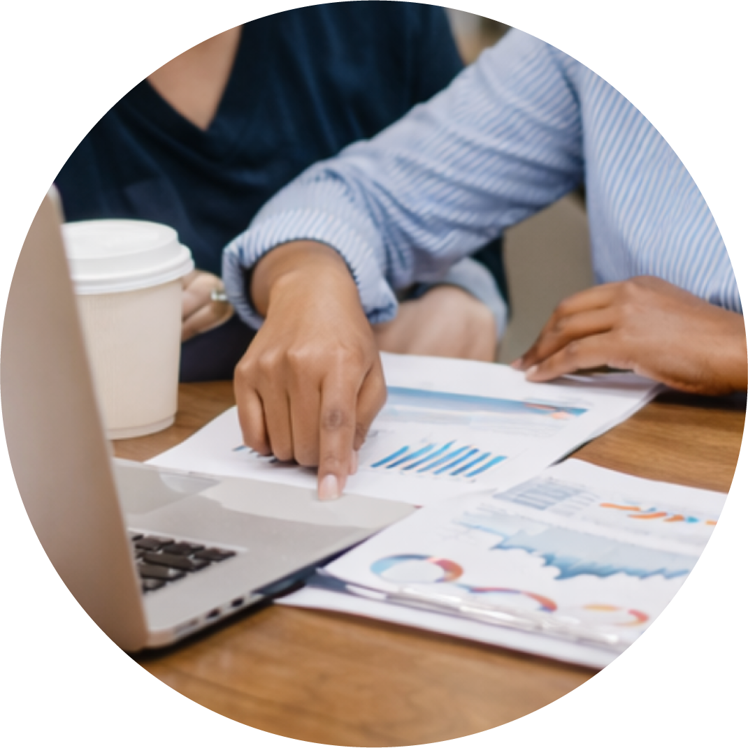 Woman's hand pointing to a laptop and paper with charts