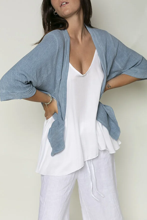 Woman wearing a white v-neck top, light blue cardigan, and white pants, posing with hands on hips against a plain background.