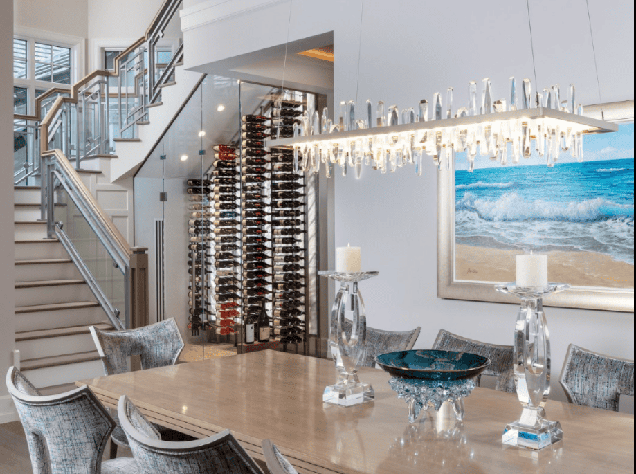 Modern dining room with a wooden table, six upholstered chairs, a large glass chandelier, a wall-mounted wine rack, and a beach painting on the wall.