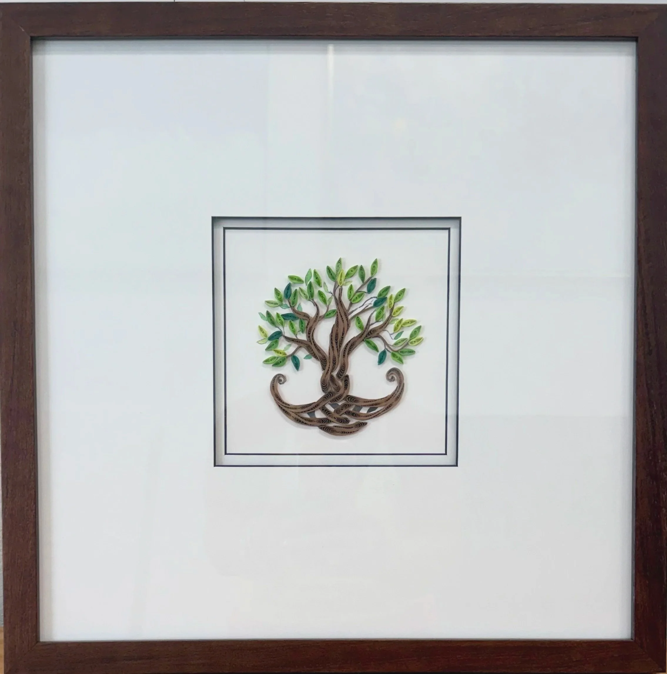 Framed artwork of a tree with green leaves, made from layered paper, mounted on a white background.