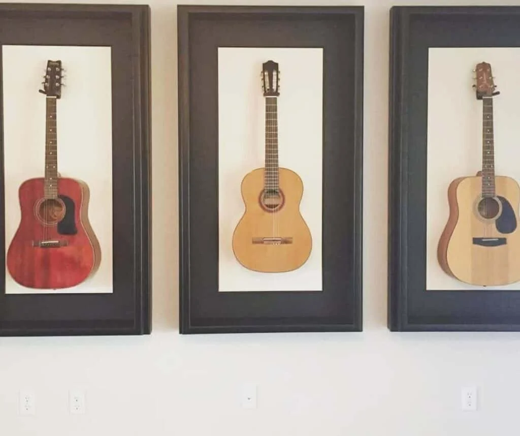 Three framed wall art pieces displaying different acoustic guitars arranged in a row.