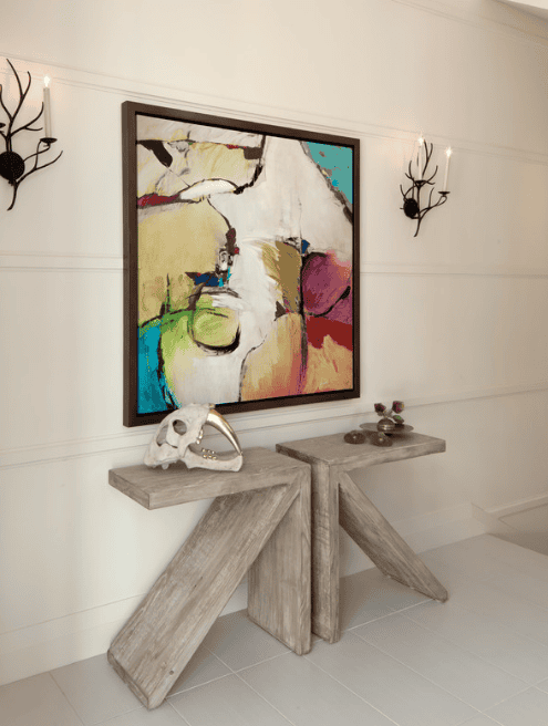 Decorative wall with two black wall sconces, abstract painting, and a wooden console table with a skull sculpture and small decorative items.