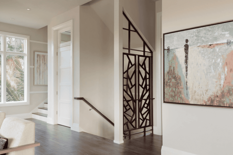 Interior view of a modern home with a staircase, large window, decorative wall art, and a geometric room divider.