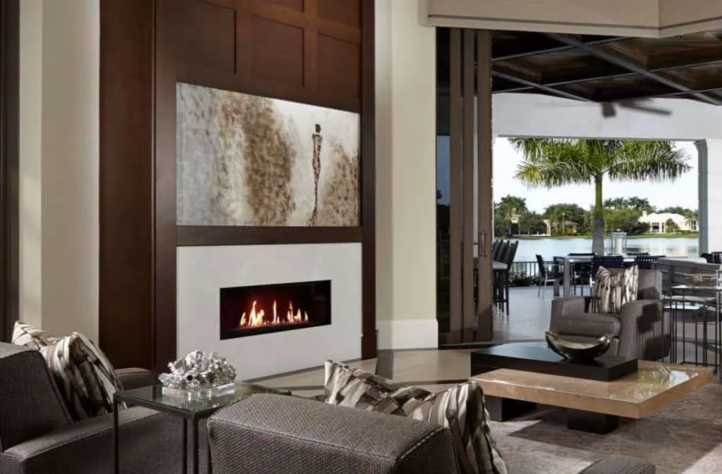 Living room with a fireplace, modern furniture, and a view of a lake with palm trees outside.