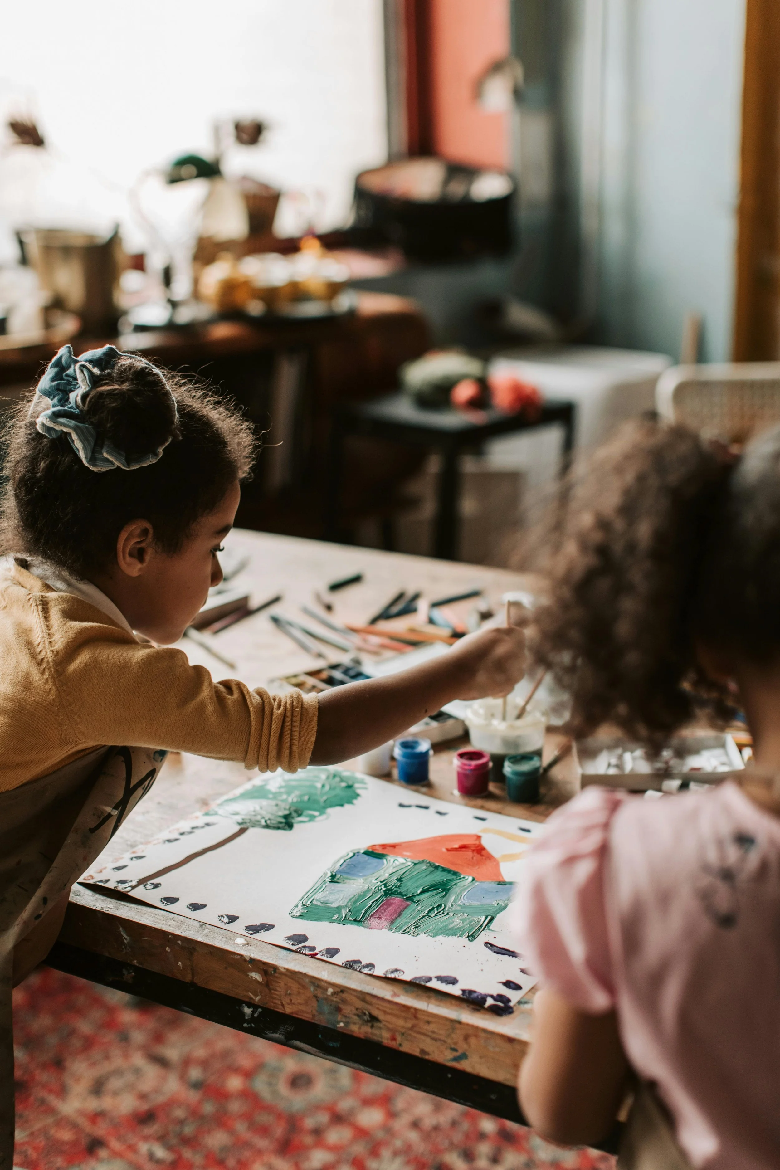 Children engaged in painting activities at a craft table in a cozy, well-lit room.