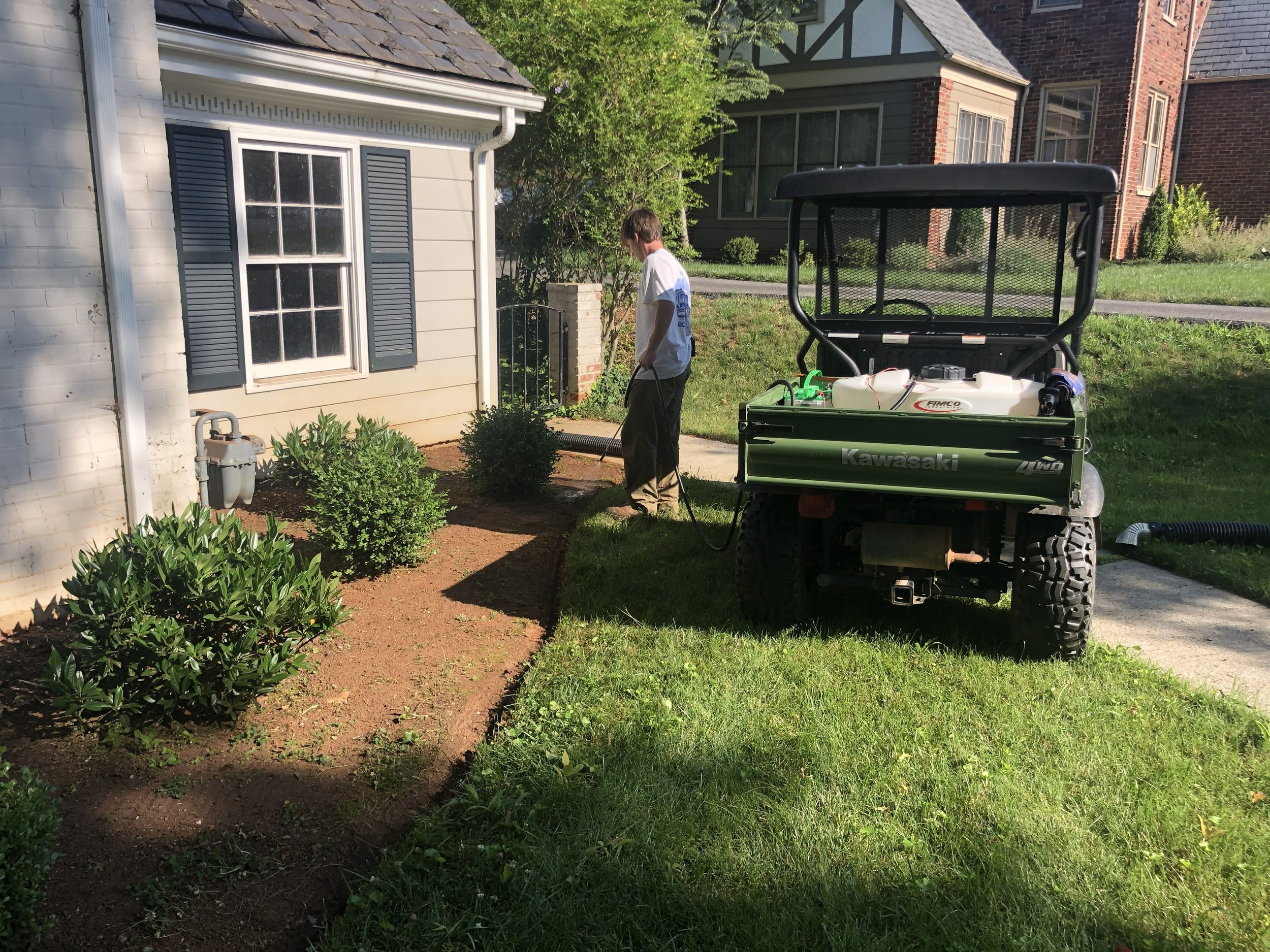 Oakwood Landscapes crew member utilizing a garden sprayer to water new plants and in bushes in a mulch bed located in Richmond, VA.