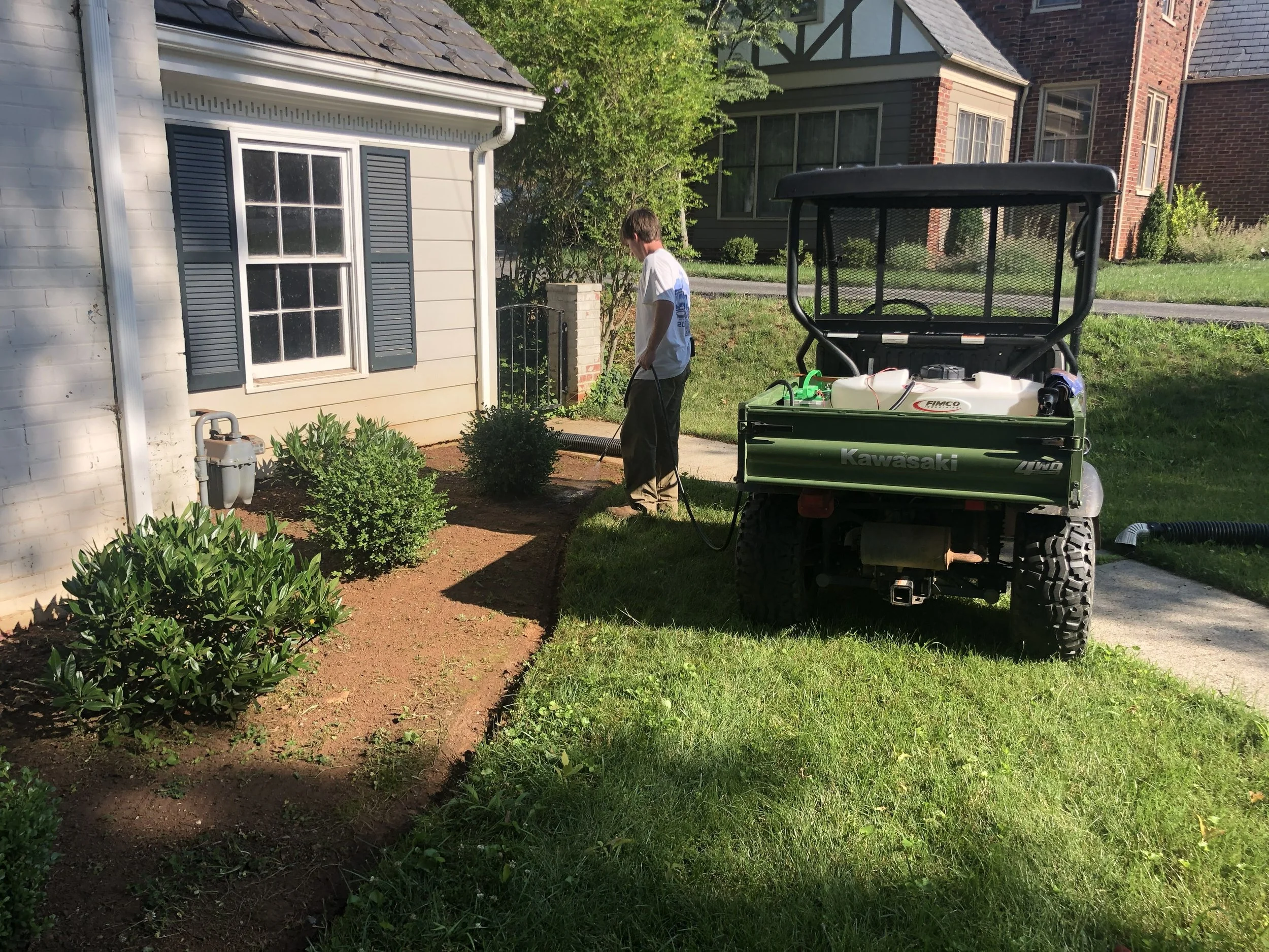 Oakwood Landscapes crew member utilizing a garden sprayer to water new plants and in bushes in a mulch bed located in Richmond, VA.