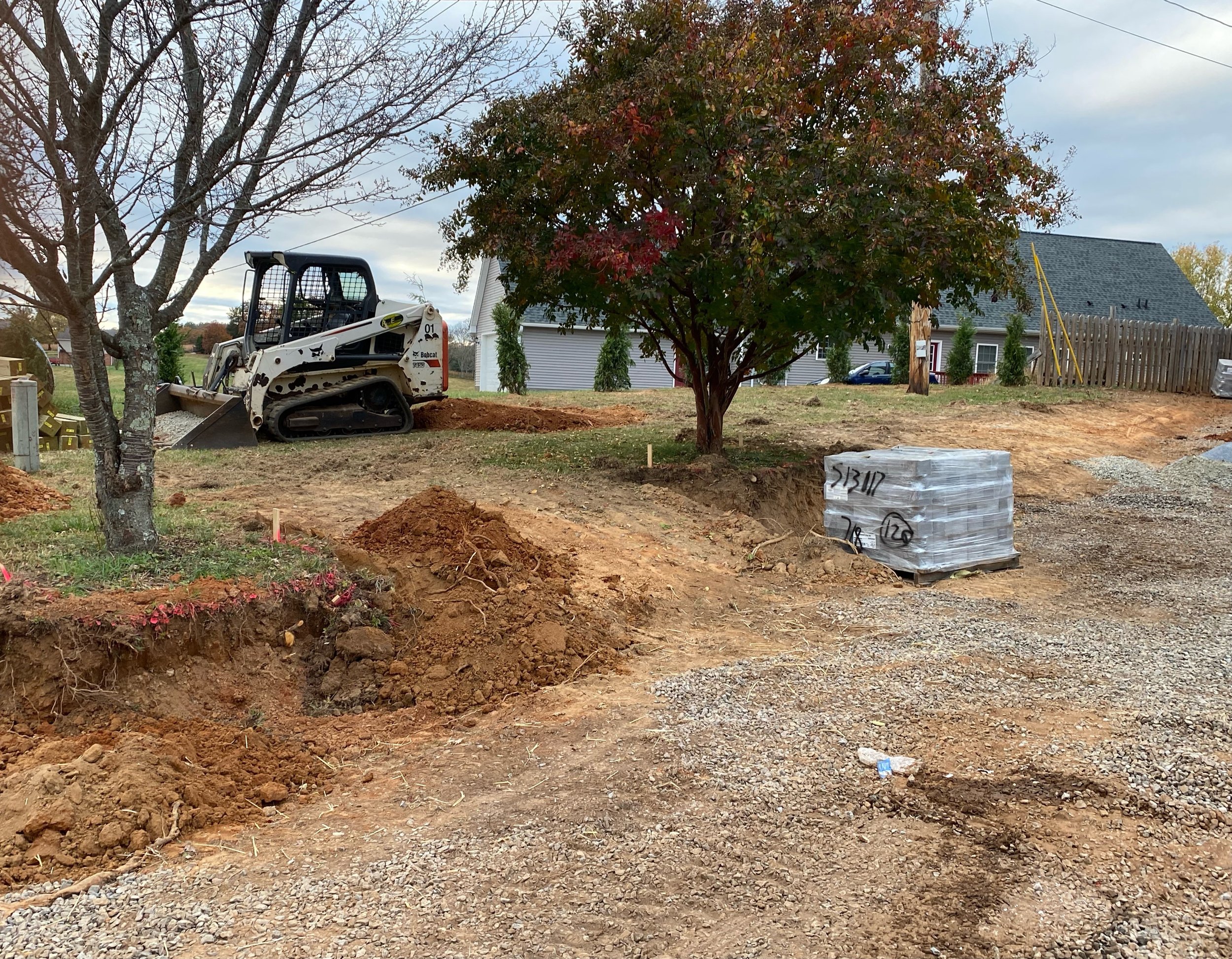 Retaining wall excavation site with segmental retaining wall blocks and a skid-street machine with a bucket.