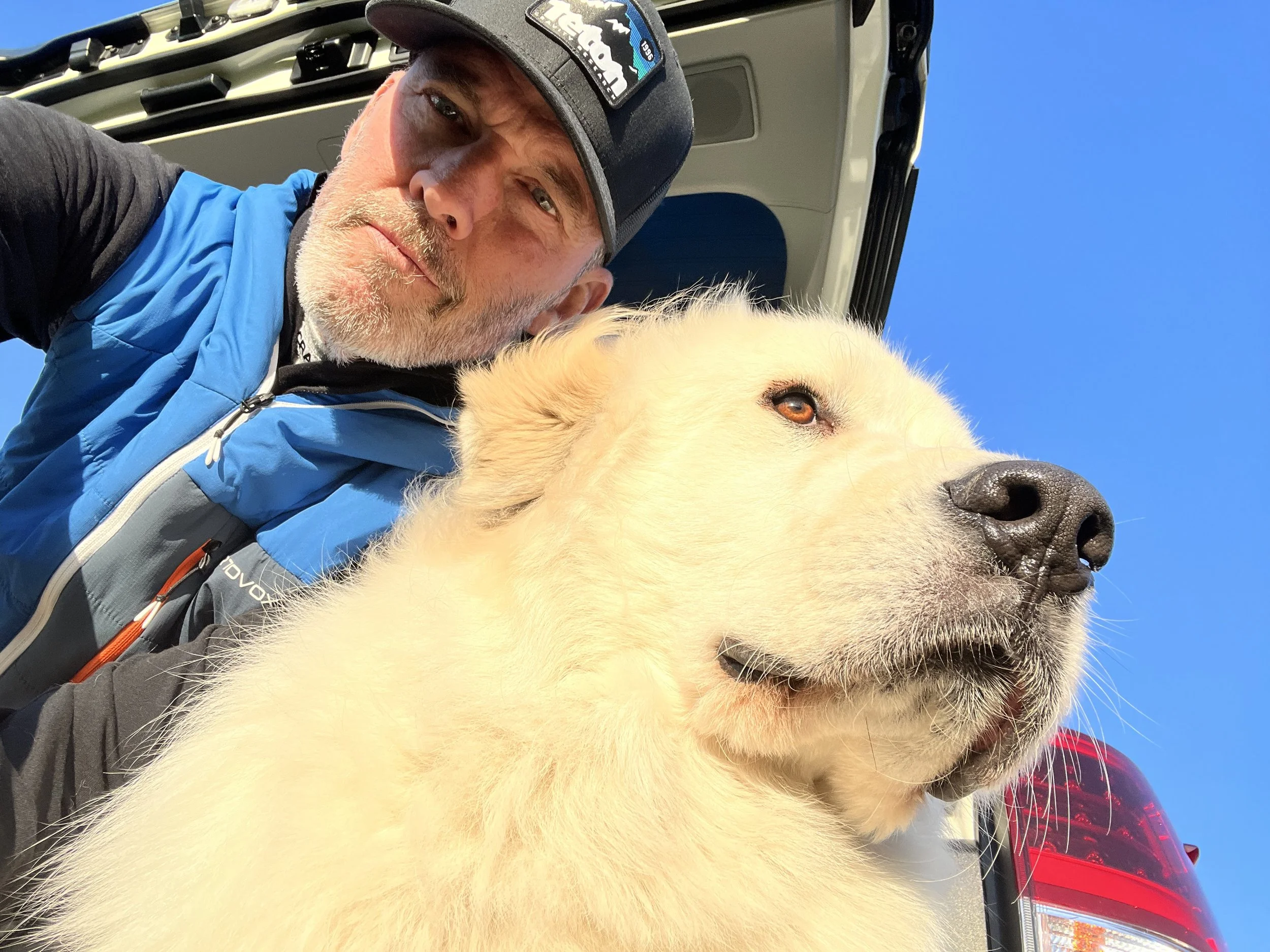 A dog trainer wearing a black cap with a TGR logo taking a selfie with a Great Pyrennes.