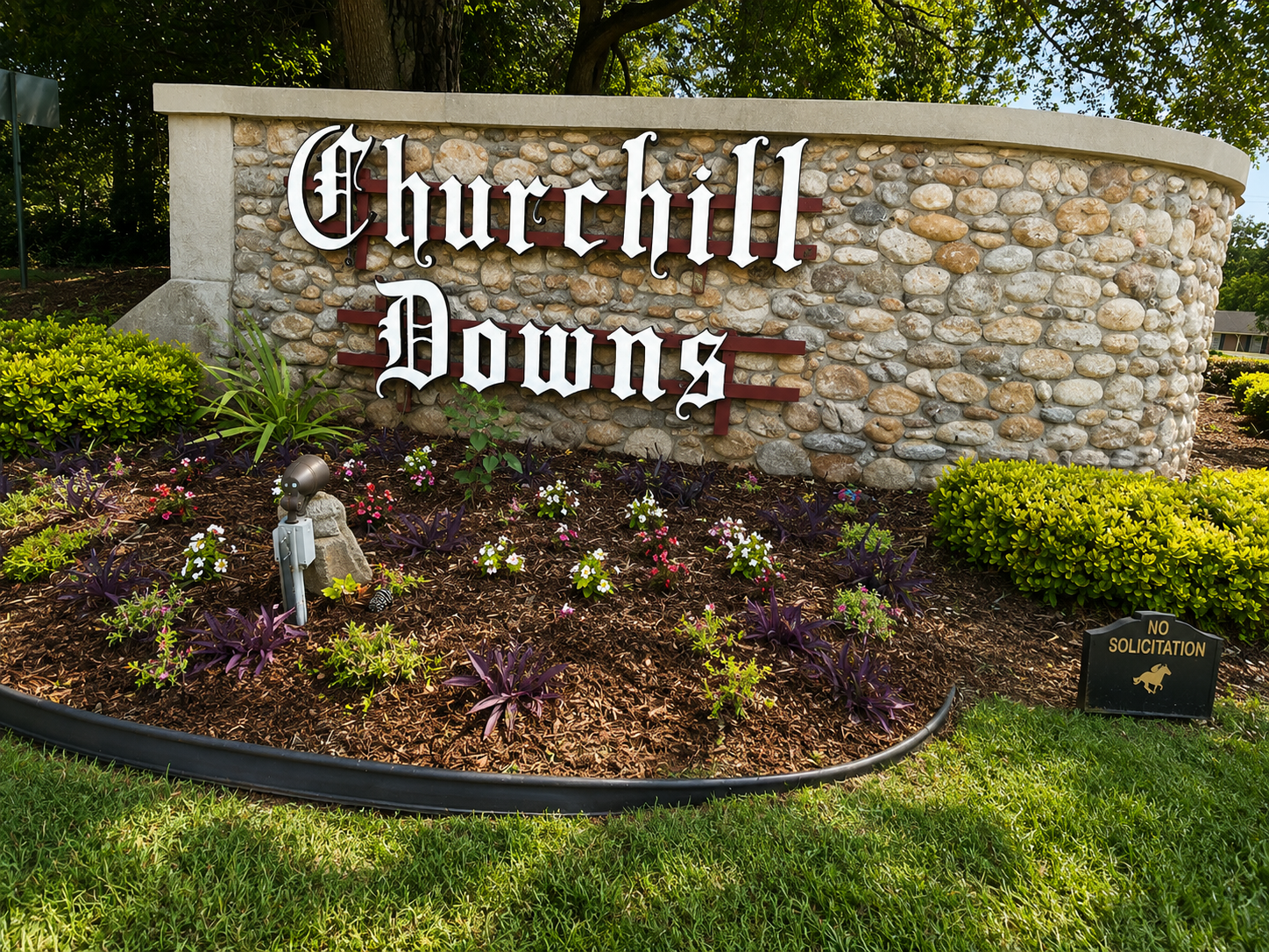Stone sign reading 'Churchill Downs' with flower bed in front and bushes on the sides, and a small sign saying 'No Solicitation' with a gold horse silhouette.