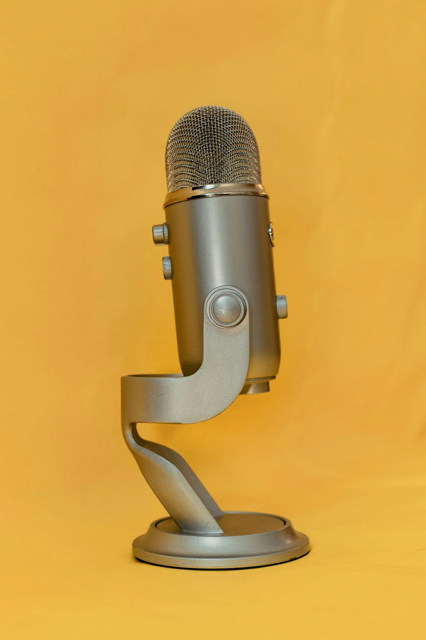 A silver microphone with a textured grill and a stand against a yellow background.